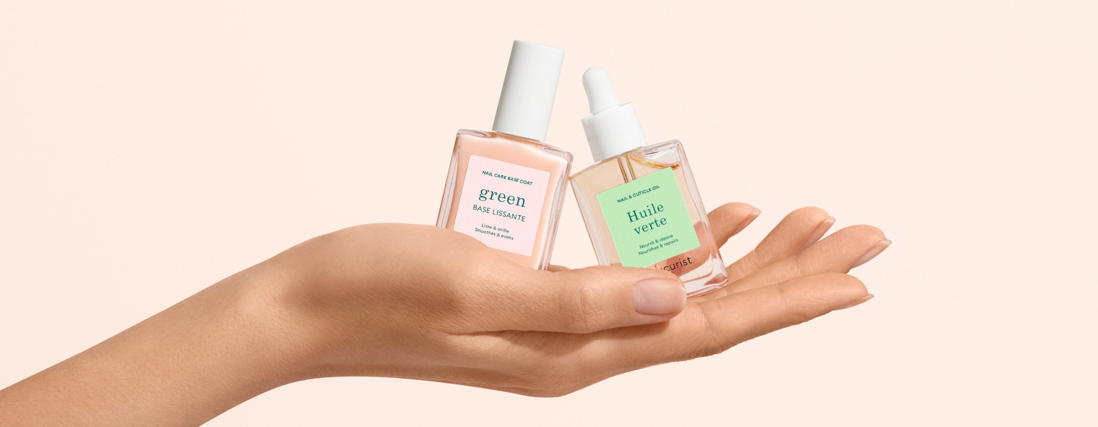 A hand holds two glass bottles of facial serums with dropper tops and green labels against a light beige background. One label reads green and the other reads Huile verte.