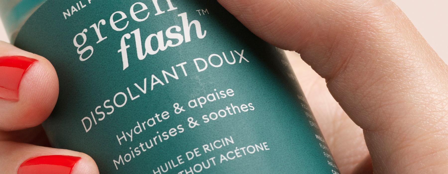 A hand with red nail polish holds a green bottle labeled Green Flash Dissolvant Doux, which hydrates, soothes, and moisturizes without acetone.