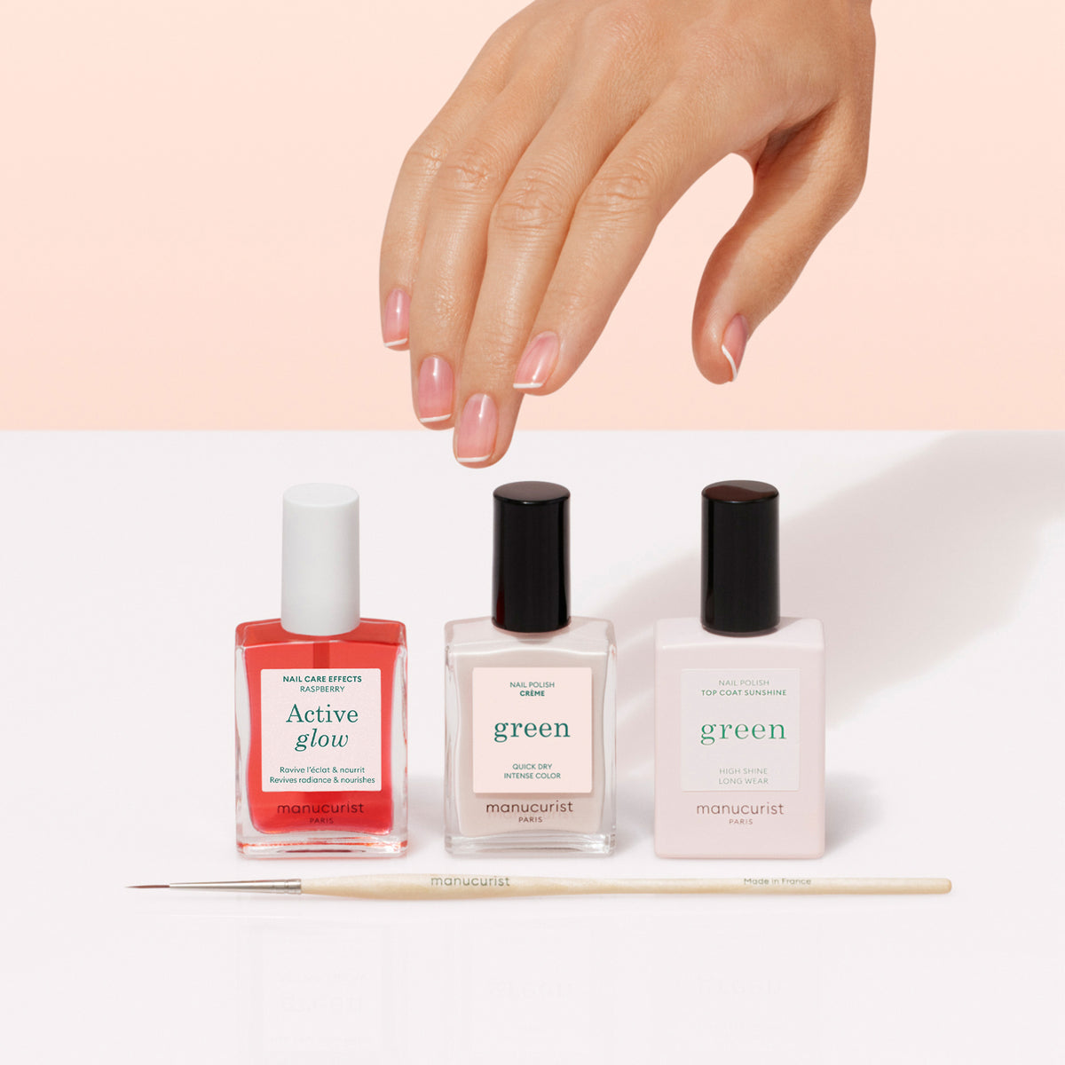 Une main aux ongles manucurés est posée au-dessus de trois flacons de vernis Manucurist French Manicure Glow et d&