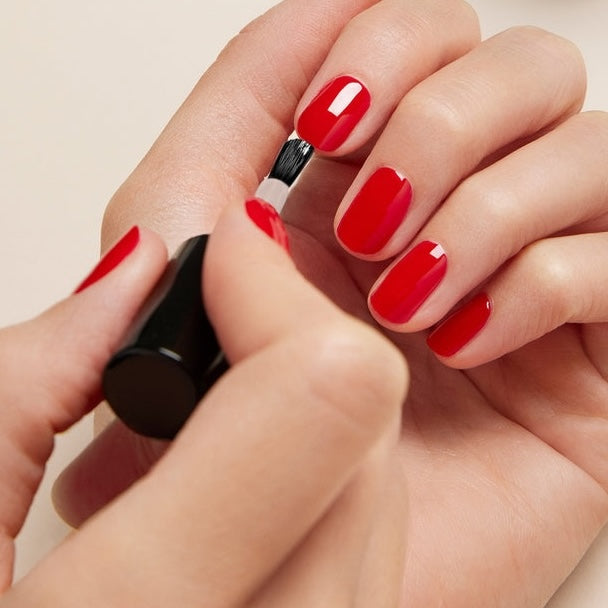 Une personne applique le Top Coat Green Sunshine de Manucurist sur ses ongles, tenant un pinceau dans une main et vernissant des ongles déjà partiellement colorés pour un effet gel brillant et biosourcé.