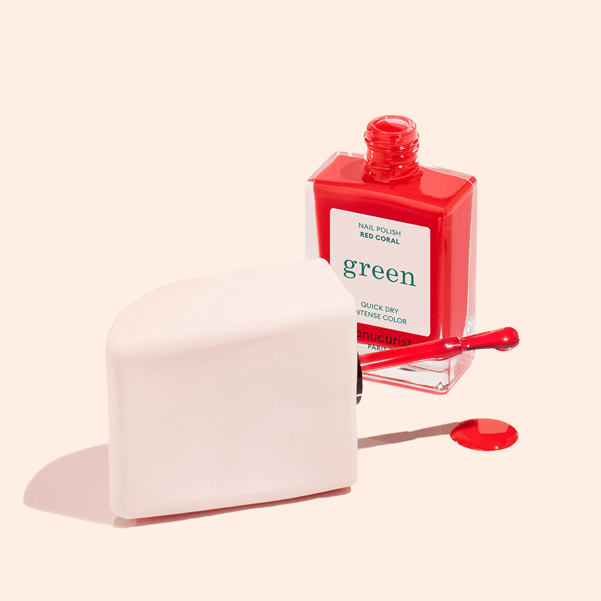 A bottle of Manucurist US Mani Helper rests with its brush on a white object and a small drop of polish on a light peach surface—ideal for achieving a flawless manicure.