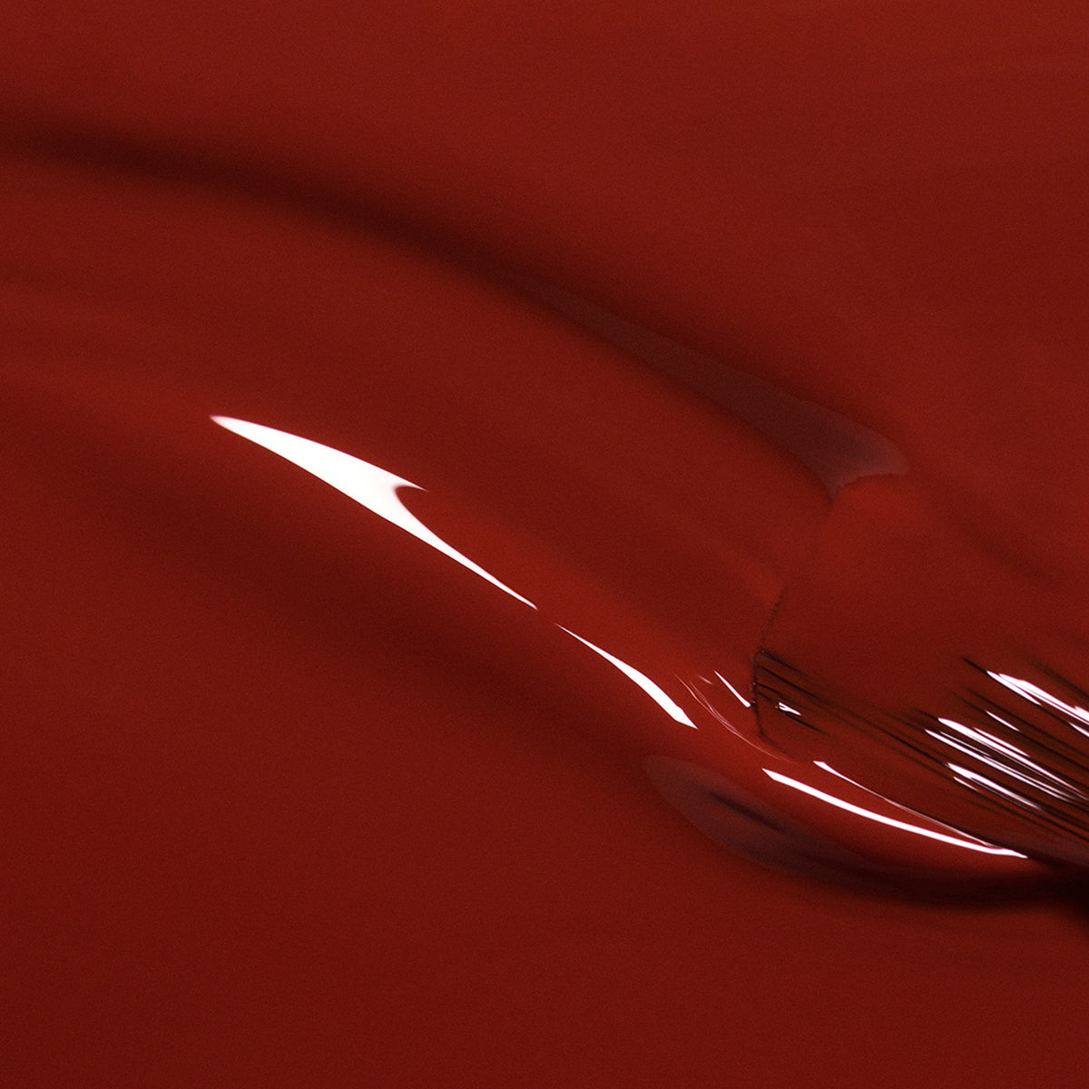 Close-up of Bohème by Manucurist—a glossy, smooth red surface with brown undertones and curved reflections, reminiscent of red polish for an abstract, fluid look.