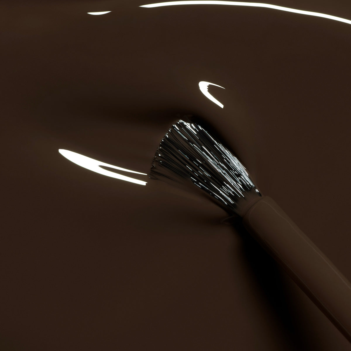 A close-up of a Manucurist Mocha brush dipped in smooth, glossy dark brown nail polish, with bright reflections highlighting the bristles and polish surface.