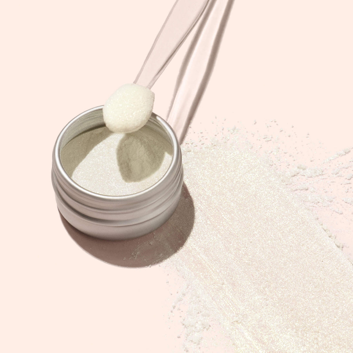 Un pot ouvert de poudre effet glacé doré Manucurist est posé sur une surface rose clair, ses reflets dorés nacrés captant la lumière. Un petit applicateur et un peu de poudre renversée en font l&