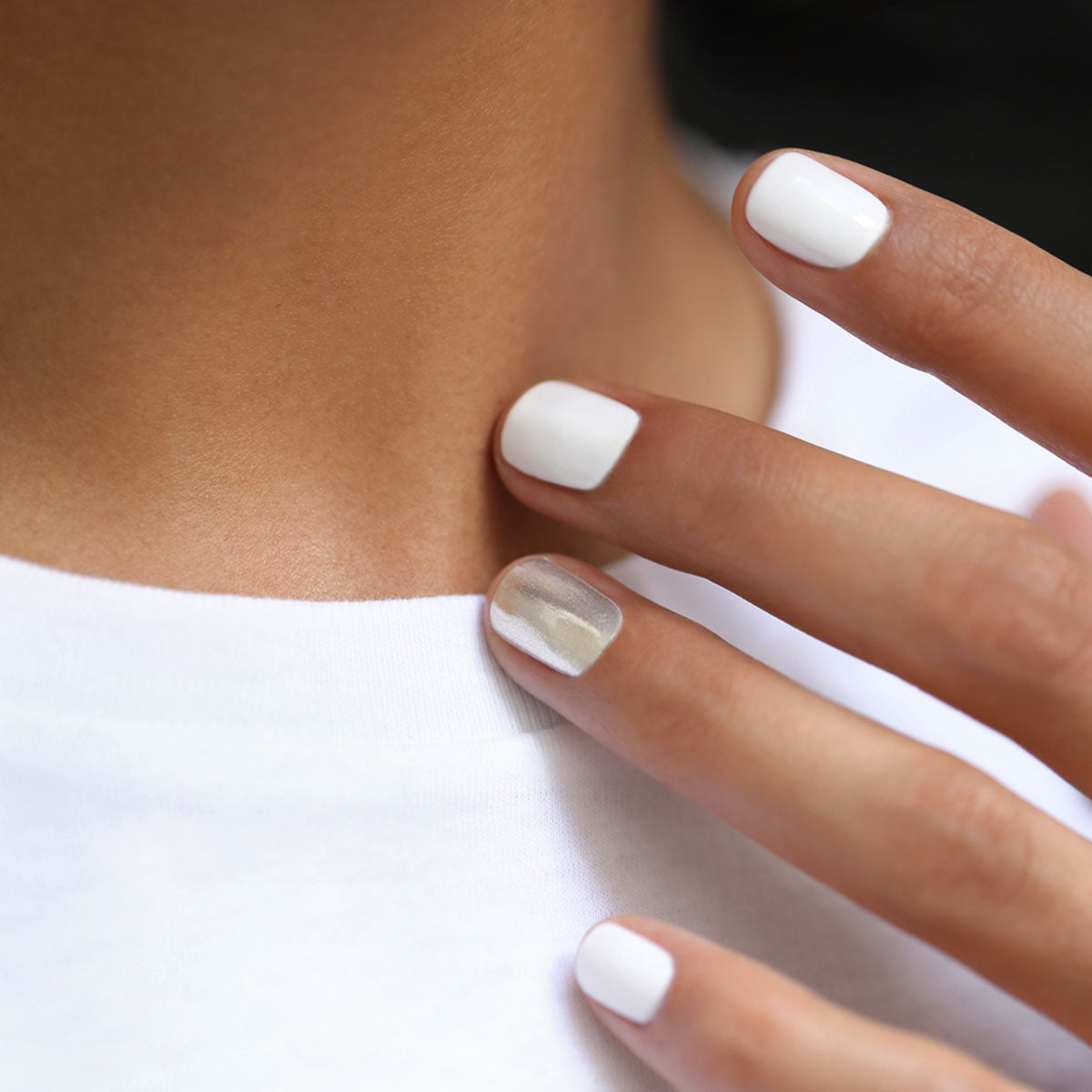 A close-up of neatly manicured nails painted with the Manucurist Red, White Blue Trio, gently touching a collarbone, complements striking red, white, and blue eyeshadow for a bold look.