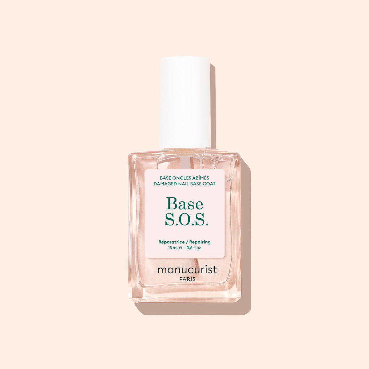 Un flacon transparent de Durcisseur S.O.S. Manucurist avec un bouchon blanc repose sur un fond beige clair, arborant une étiquette en français et en anglais indiquant "Répare régénère" — parfait pour les ongles cassants nécessitant d&