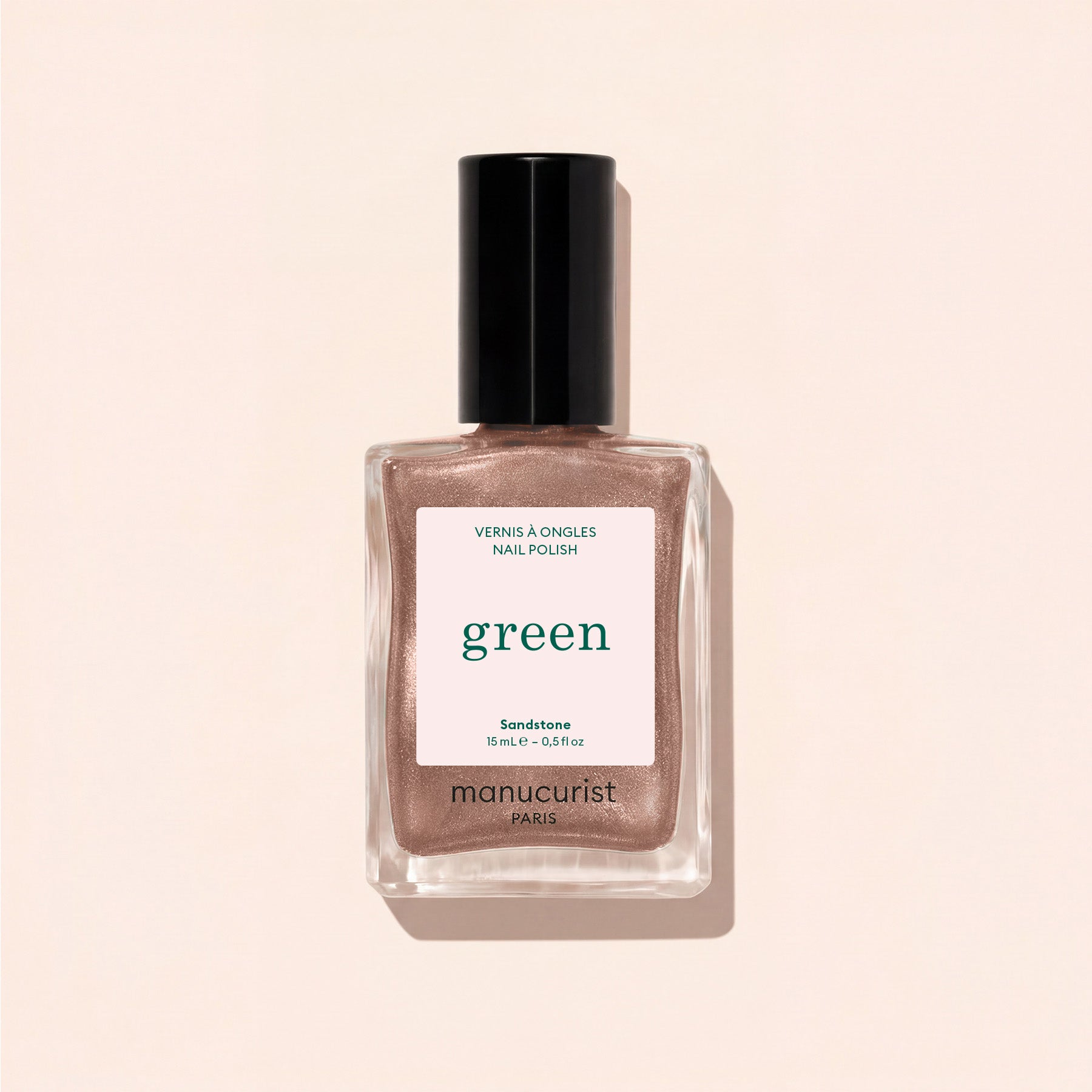 A bottle of Manucurist nail polish in the shade Sandstone, a shimmery rose gold hue, displayed against a light beige background.
