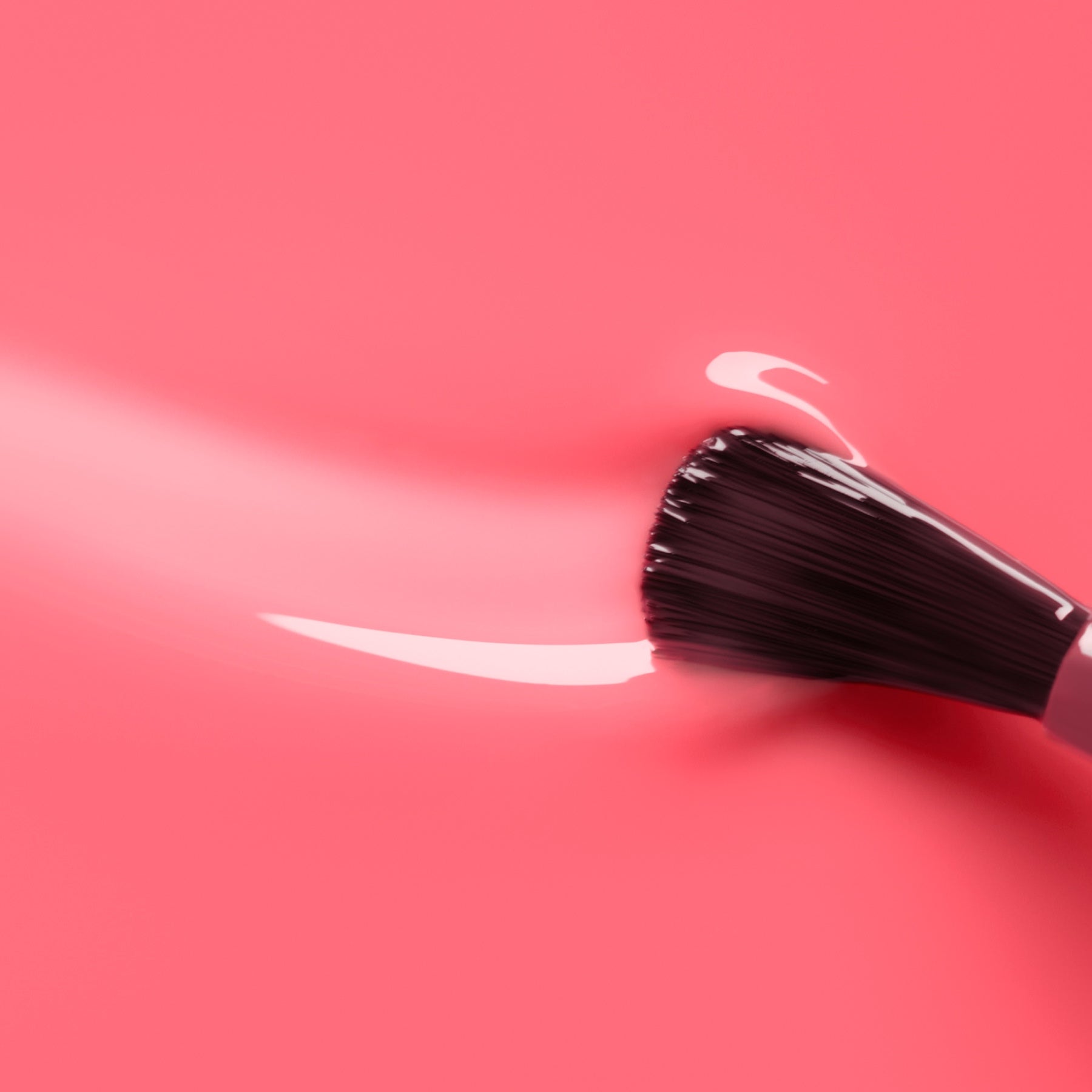 A Manucurist Sugar Plum makeup brush with black bristles glides glossy, translucent pink polish over a smooth, vibrant pink surface, leaving a curved streak behind.