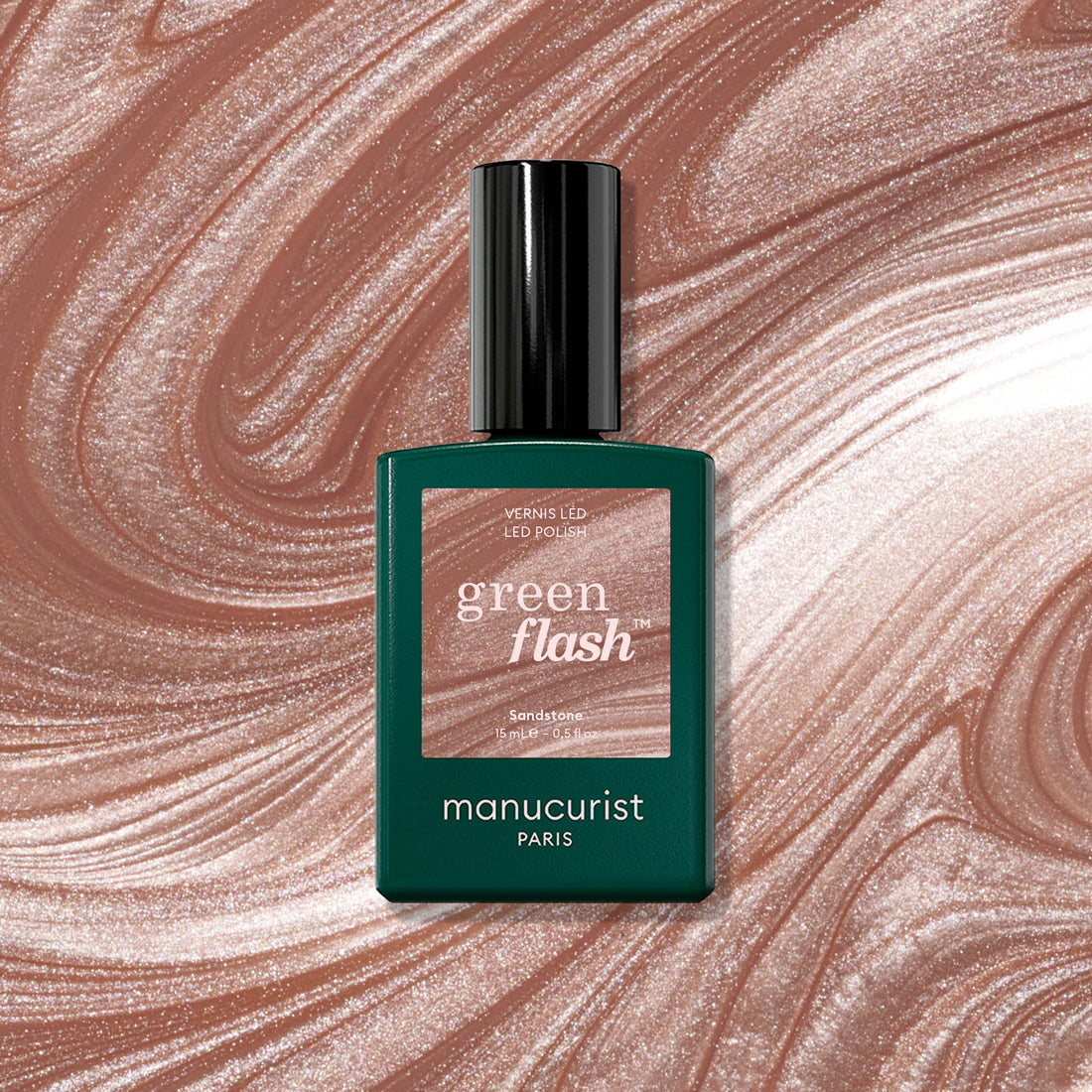 A bottle of Manucurist Sandstone rests on a swirling, shimmering marbled background in shades of latte brown and beige.