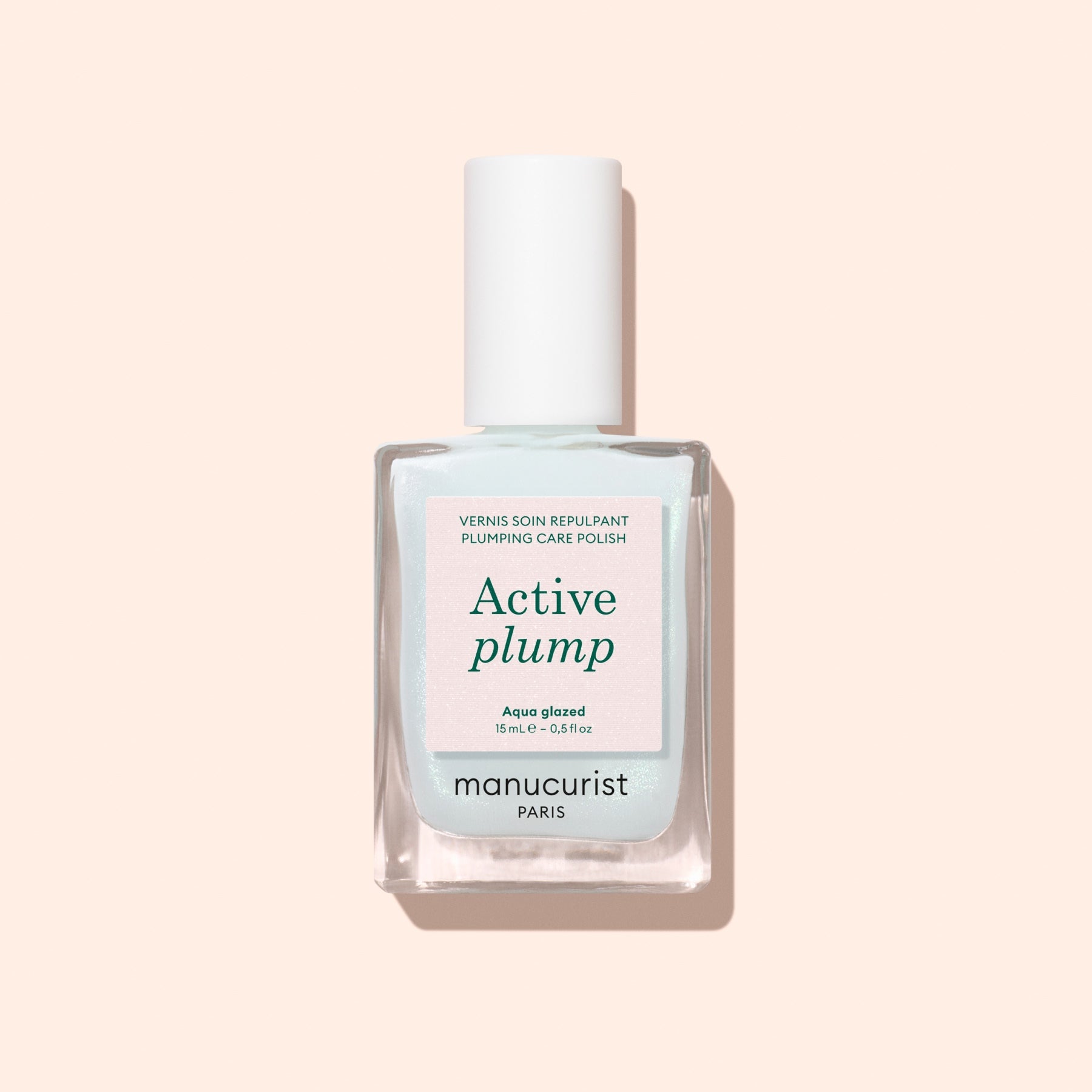 A bottle of Manucurist Active Plump Aqua Glazed nail polish with a white cap sits on a light beige background. The pale blue and white label features green and pink text, highlighting hydration for beautifully healthy nails.