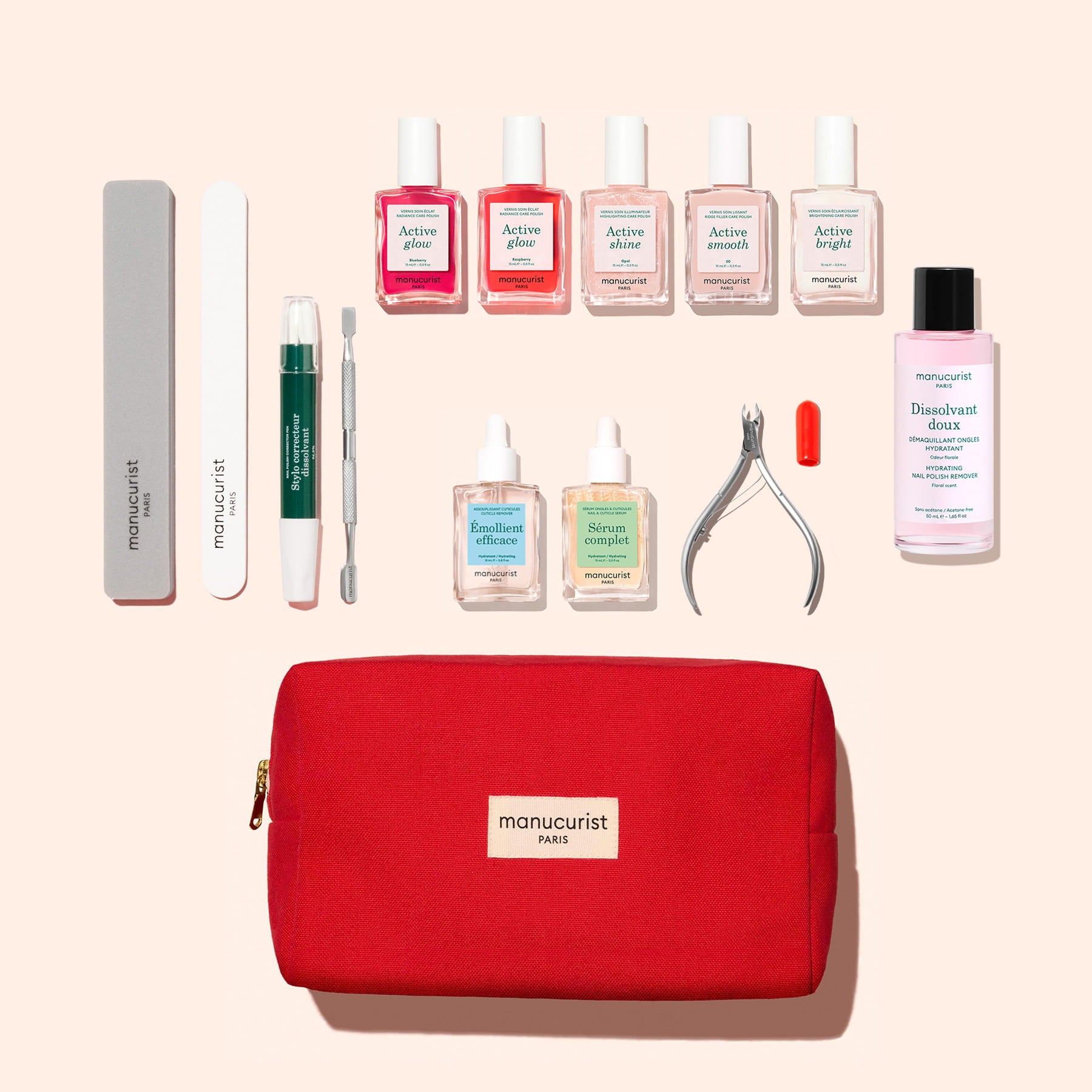 The Manucurist Super Ultimate Active Manicure Kit, featuring a red bag, comes with nail files, a cuticle pusher, polishes, serums, nail clippers, a small pill-shaped tool, and a bottle of cuticle remover—all essentials for comprehensive nail care—neatly arranged on a light background to support healthy nails.