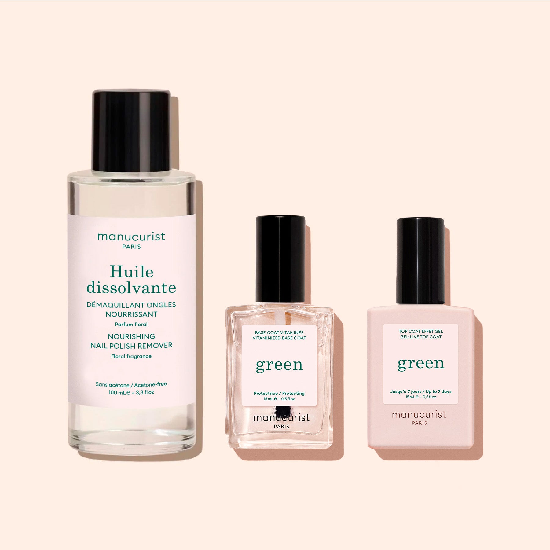 Three manicure products from Manucurist: a tall bottle of Nail Polish Removing Oil—nourishing, plant-based, and acetone-free—a square bottle of protective base coat, and another square bottle labeled "top coat" polish, all featuring black caps and set against a light beige background.