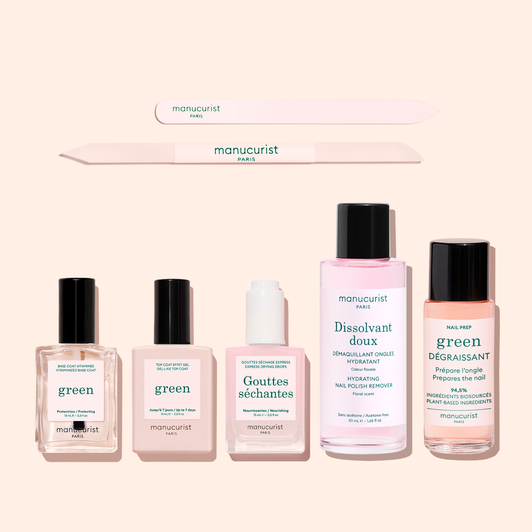 Six products from Manucurist’s "The Essentials of the Green™ System," including a nail file, gel effect manicure, plant-based nail polish, remover, drops, and degreaser, are arranged on a pale background. Each item showcases minimalist packaging in green and pink tones with Manucurist branding and highlights acetone-free formulas.