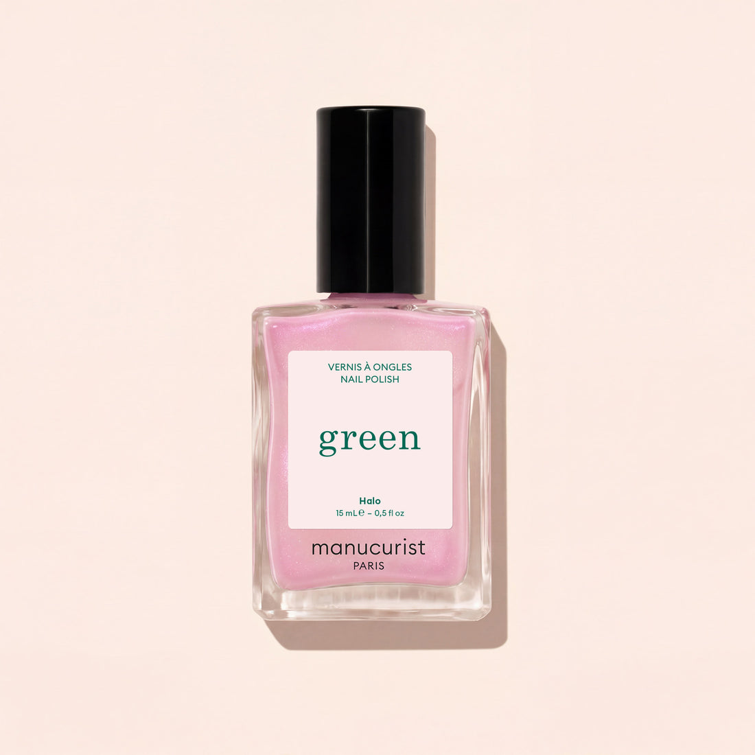 A square glass bottle of Manucurist nail polish in the shade Halo, a milky mauve color with a black cap, is shown against a light beige background.