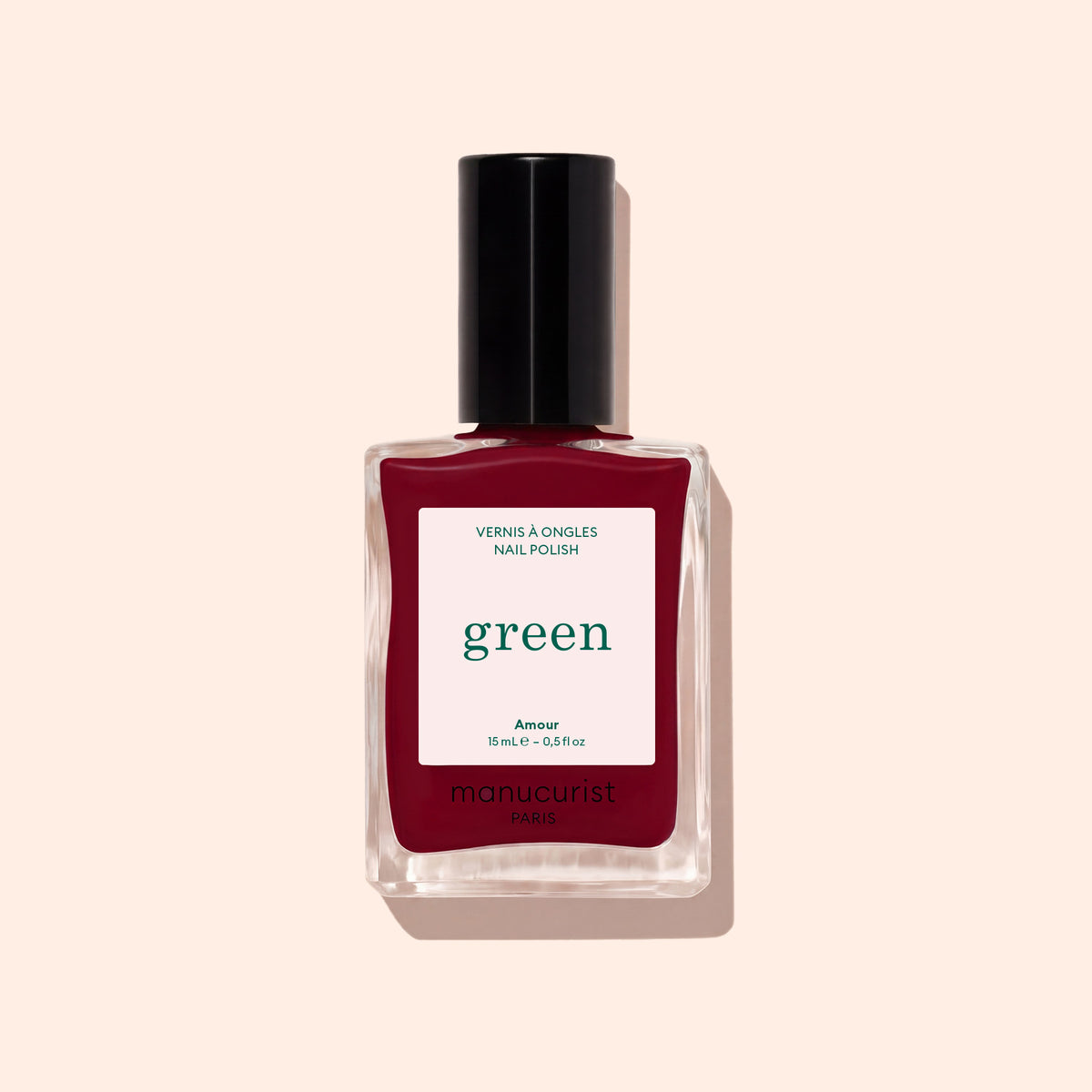 Un flacon de vernis Amour de Manucurist, une teinte bordeaux lumineuse de la gamme Green™, avec un bouchon noir et une étiquette blanche portant les mentions « green » et « Paris », présenté sur un fond beige pâle.