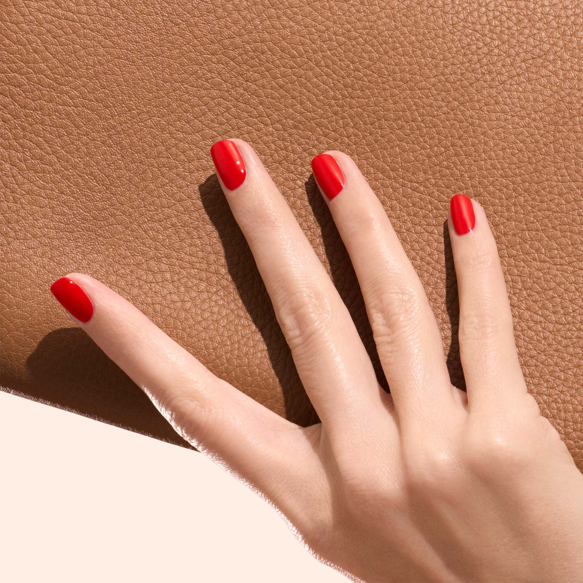 A hand with neatly manicured nails painted in Anémone by Manucurist rests on textured brown leather.