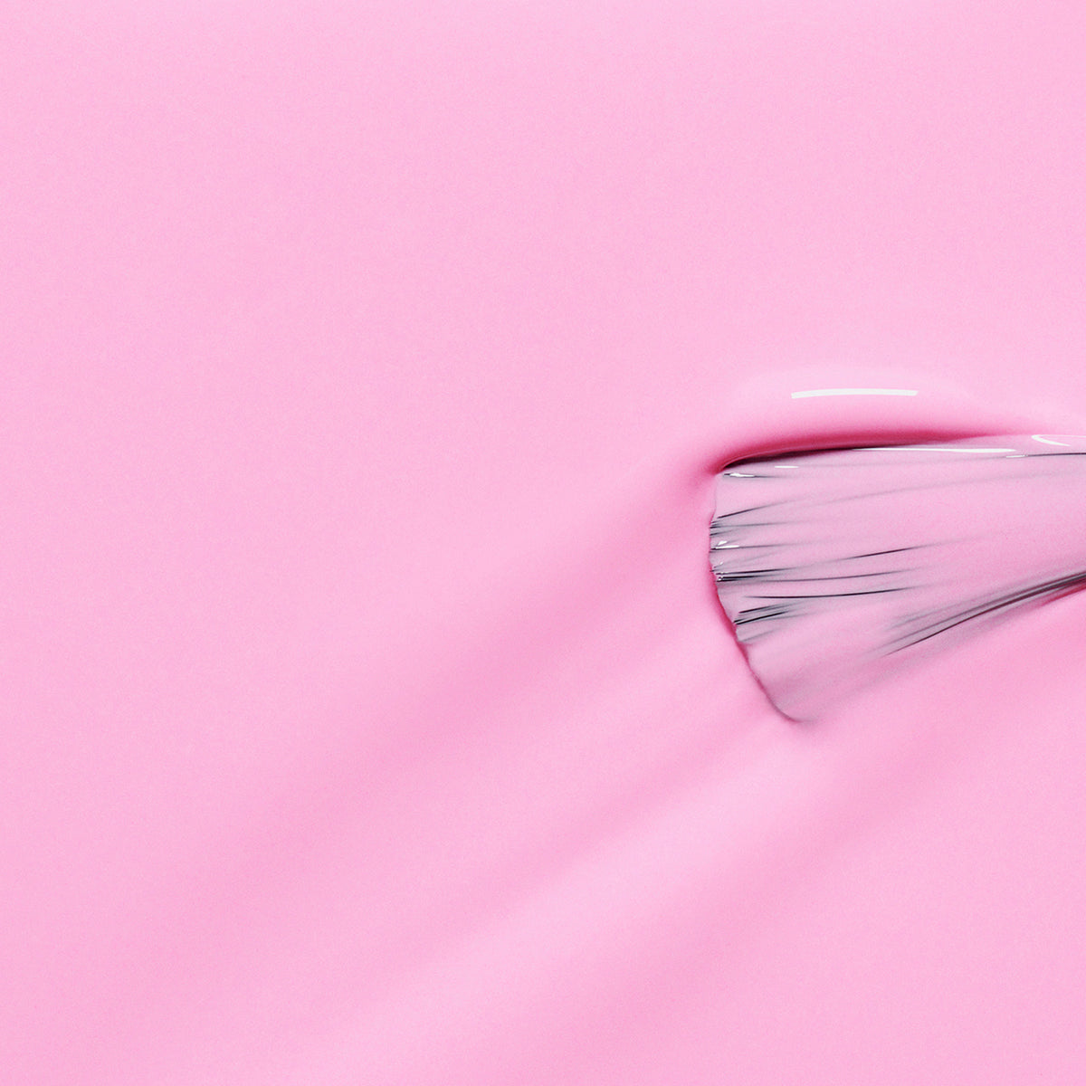 Gros plan sur le pinceau Candy de Manucurist étalant un vernis à ongles rose néon lisse et brillant, créant une texture subtile sur un fond rose uni.