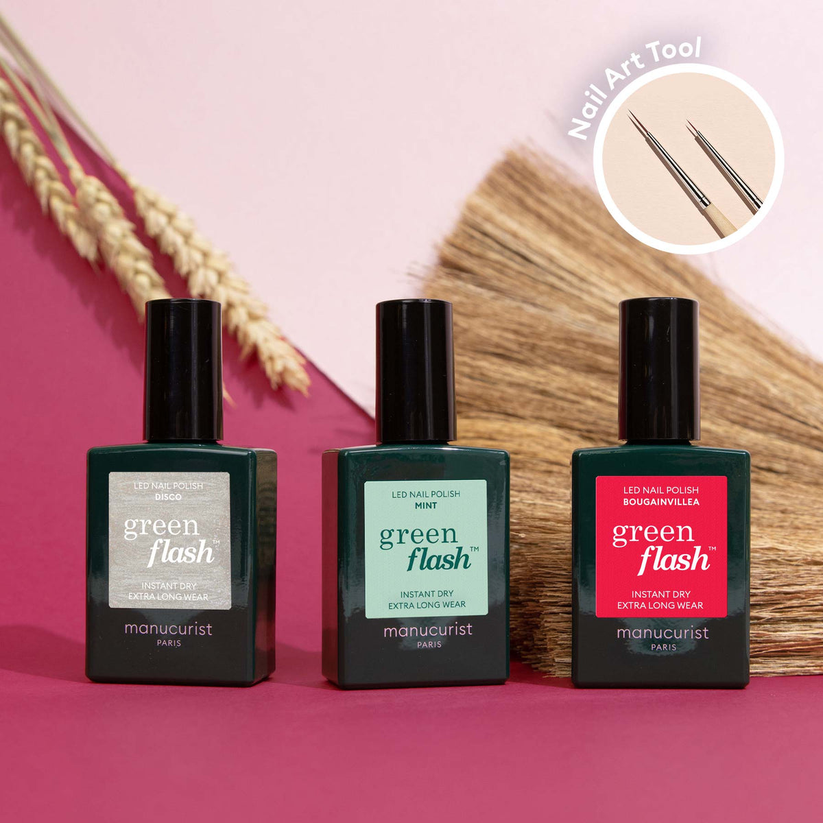 Trois flacons de vernis Manucurist Coral Reef sont disposés sur une surface rose, avec un Pinceau Nail Art en médaillon — idéal pour réaliser un nail art Coral Reef. Des plantes séchées apparaissent en arrière-plan.