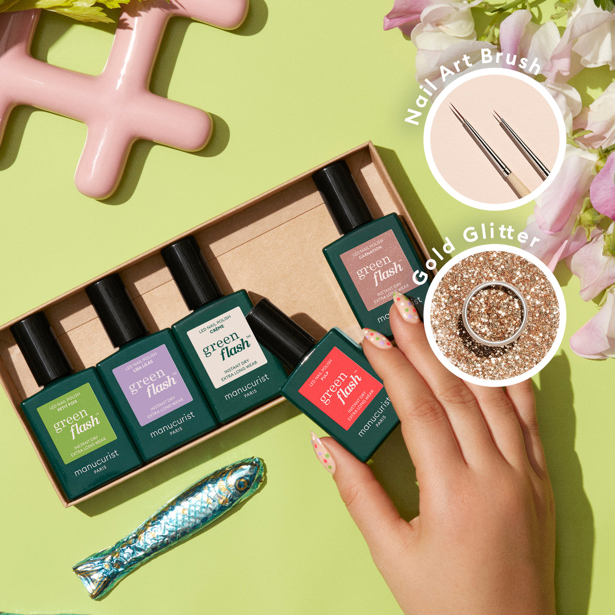 Une main choisit un flacon de vernis Manucurist Glitter in Love parmi un coffret de cinq dans une boîte, à côté d&
