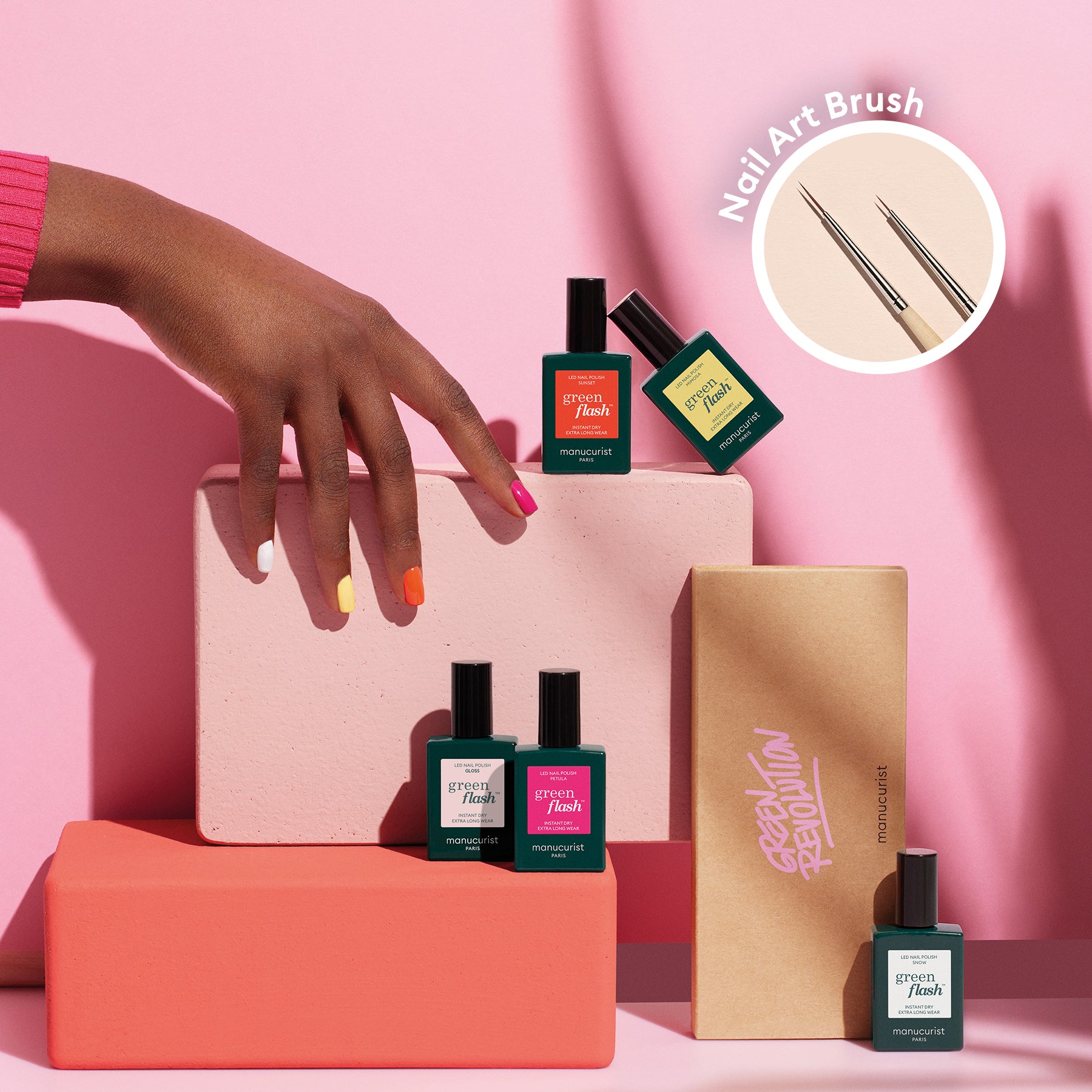 A hand with multicolored nails from Manucurist’s Smile! rests on pink and peach blocks, surrounded by four Smile! bottles and a Nail Art Brush in an inset circle—a bright, stylish setup perfect for summer nail art inspiration.