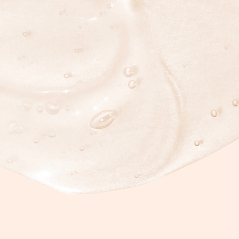 A close-up of a light peach, creamy liquid with a glossy texture and small air bubbles on a matching peach background.