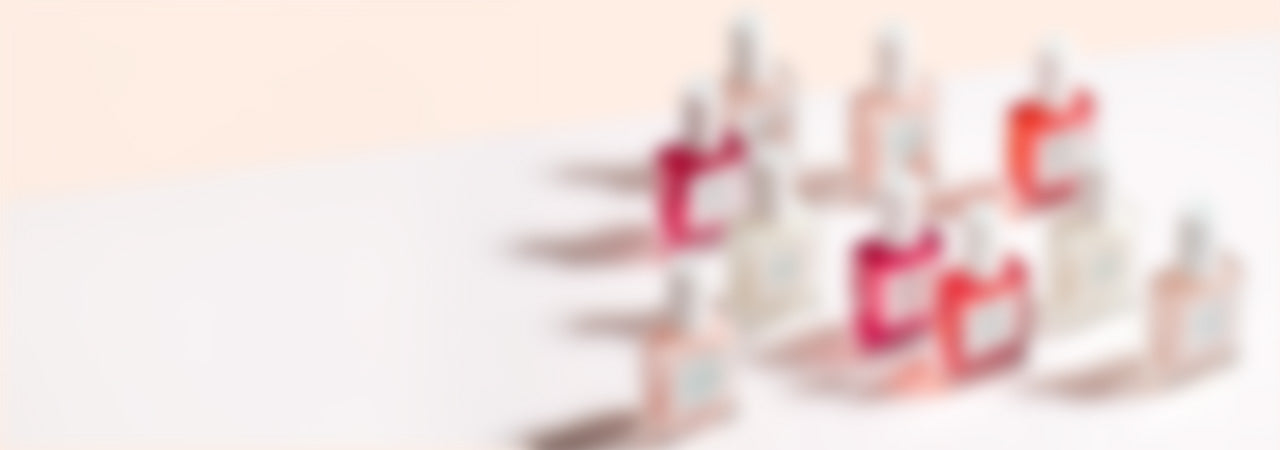A group of colorful perfume bottles is arranged on a white surface, casting soft shadows. The image is intentionally blurred, making the details of the bottles and labels indistinguishable.