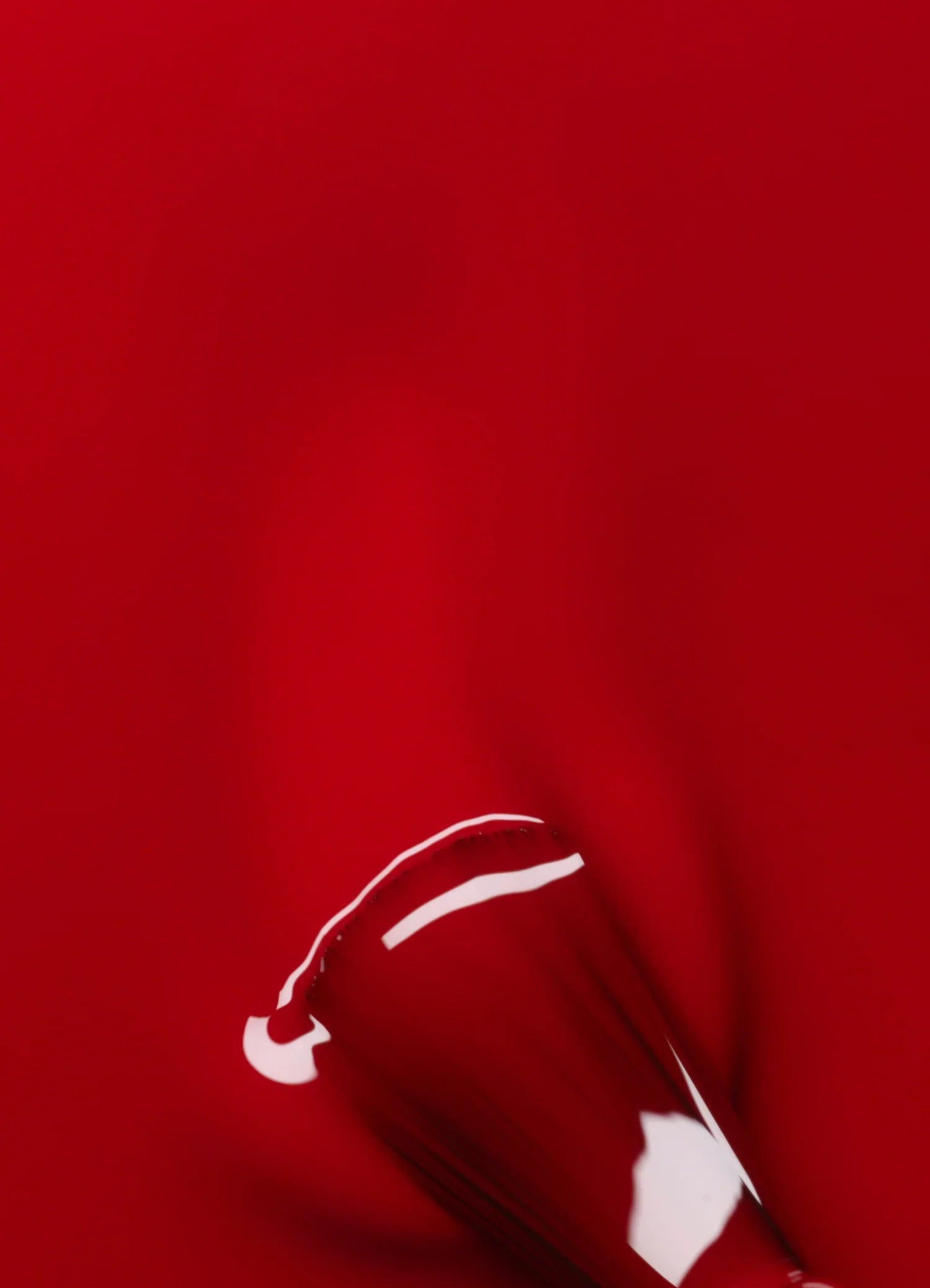 A close-up of a nail polish brush applying glossy red nail polish on a smooth, red surface.
