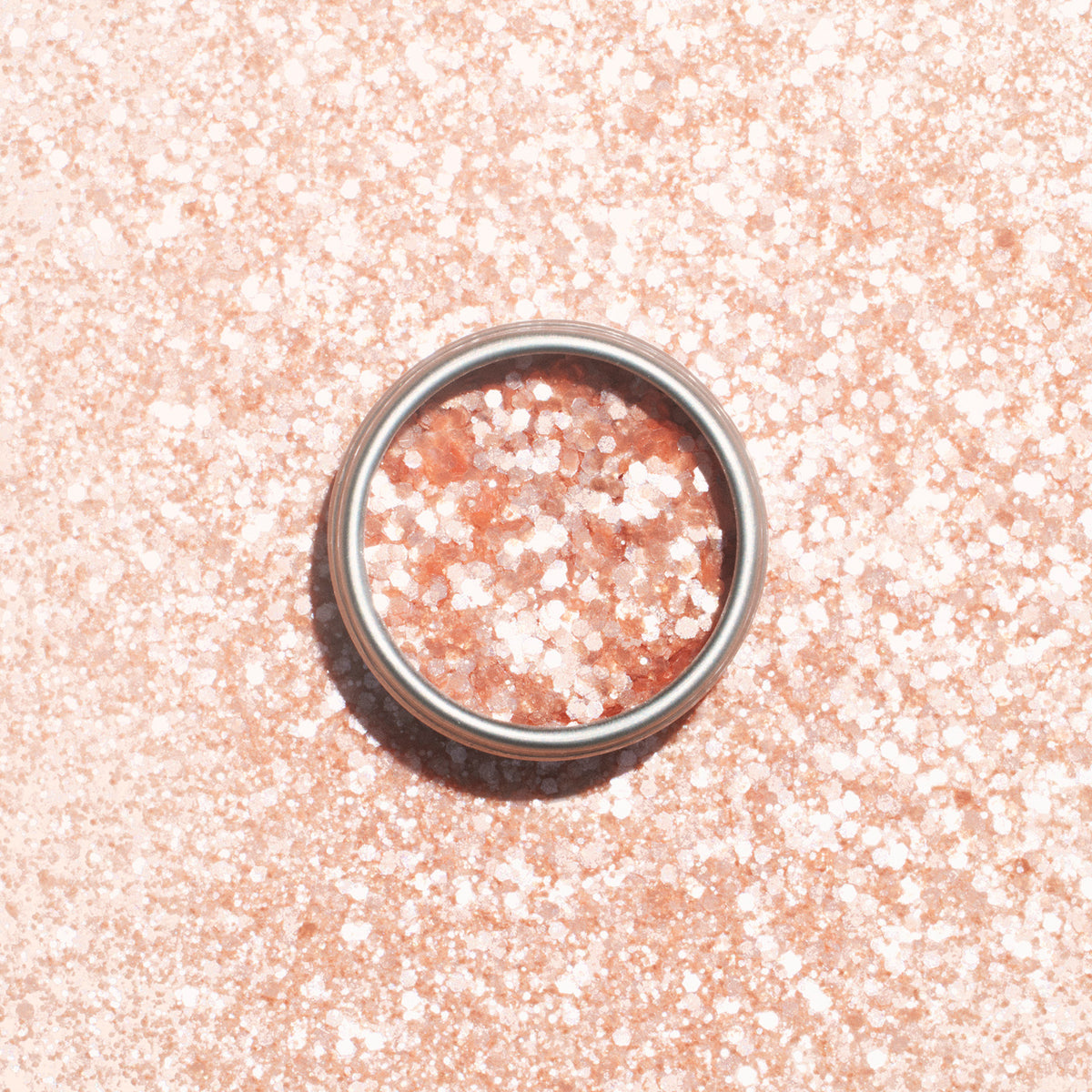 Une bague en argent repose sur une surface rose pâle parsemée de Paillettes Biodégradables Blush de Manucurist, qui scintillent à travers la bague et tout autour.