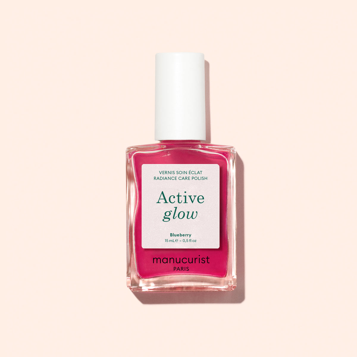 Un flacon rose de soin pour ongles d’origine végétale Manucurist Active™ Glow Blueberry avec un bouchon blanc, présenté sur un fond beige clair.