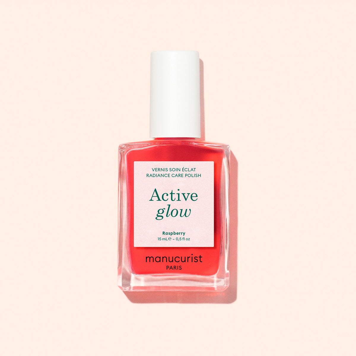 Un flacon de soin pour les ongles Active™ Glow Raspberry Manucurist, avec un bouchon blanc et une étiquette rose sur fond pêche clair, offre une nutrition d&
