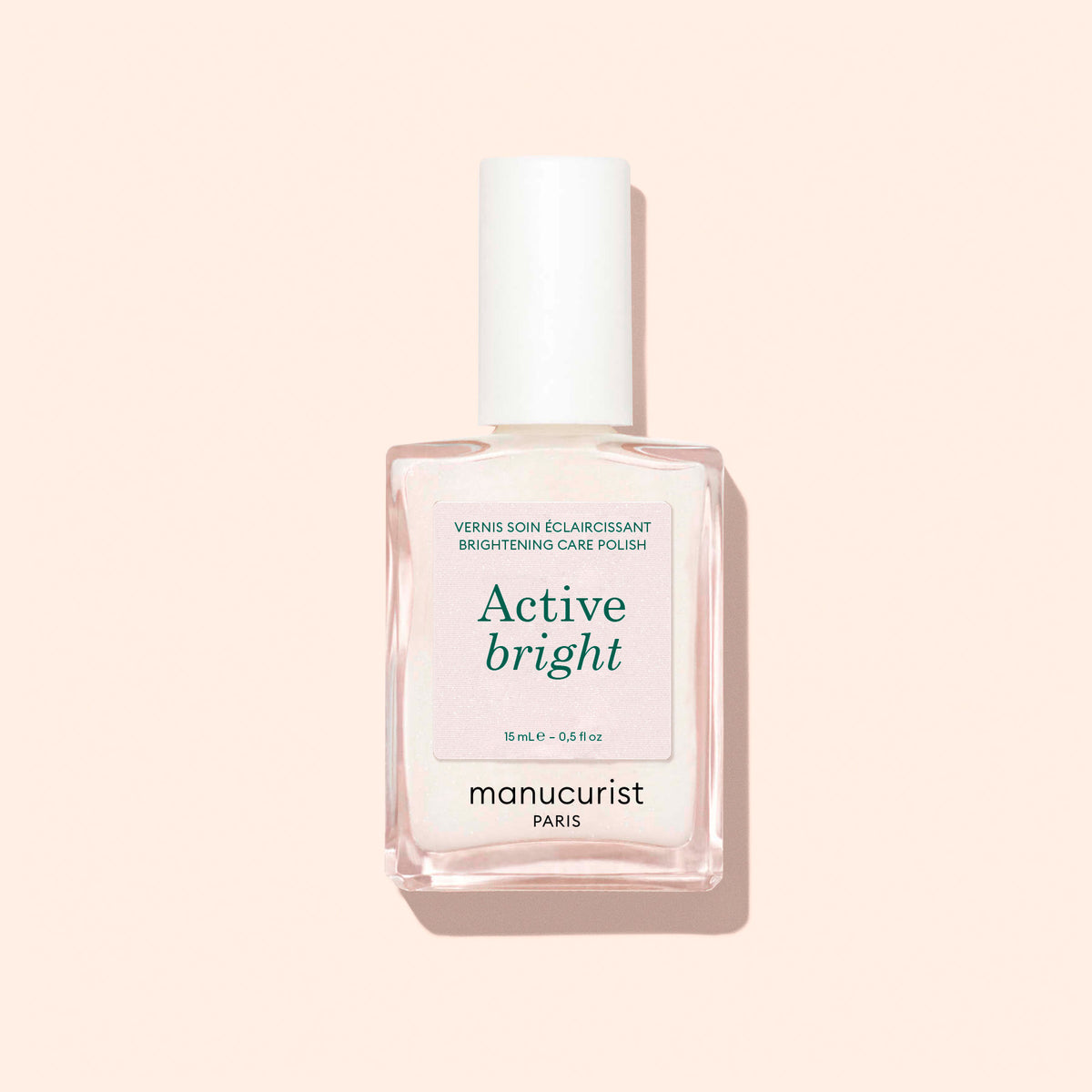 Un flacon en verre transparent de vernis à ongles Manucurist Active™ Bright, doté d’un bouchon blanc et placé sur un fond beige clair. L’étiquette indique que ce soin des ongles biosourcé illumine et renforce les ongles.