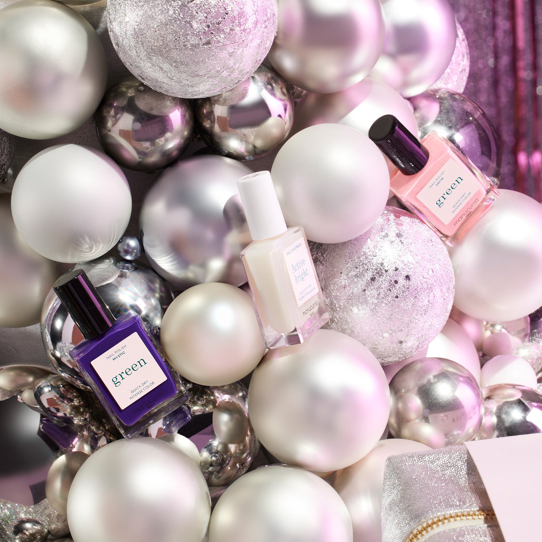 Bottles of nail polish are displayed among shiny white, silver, and glittery holiday ornaments, creating a festive and elegant arrangement.