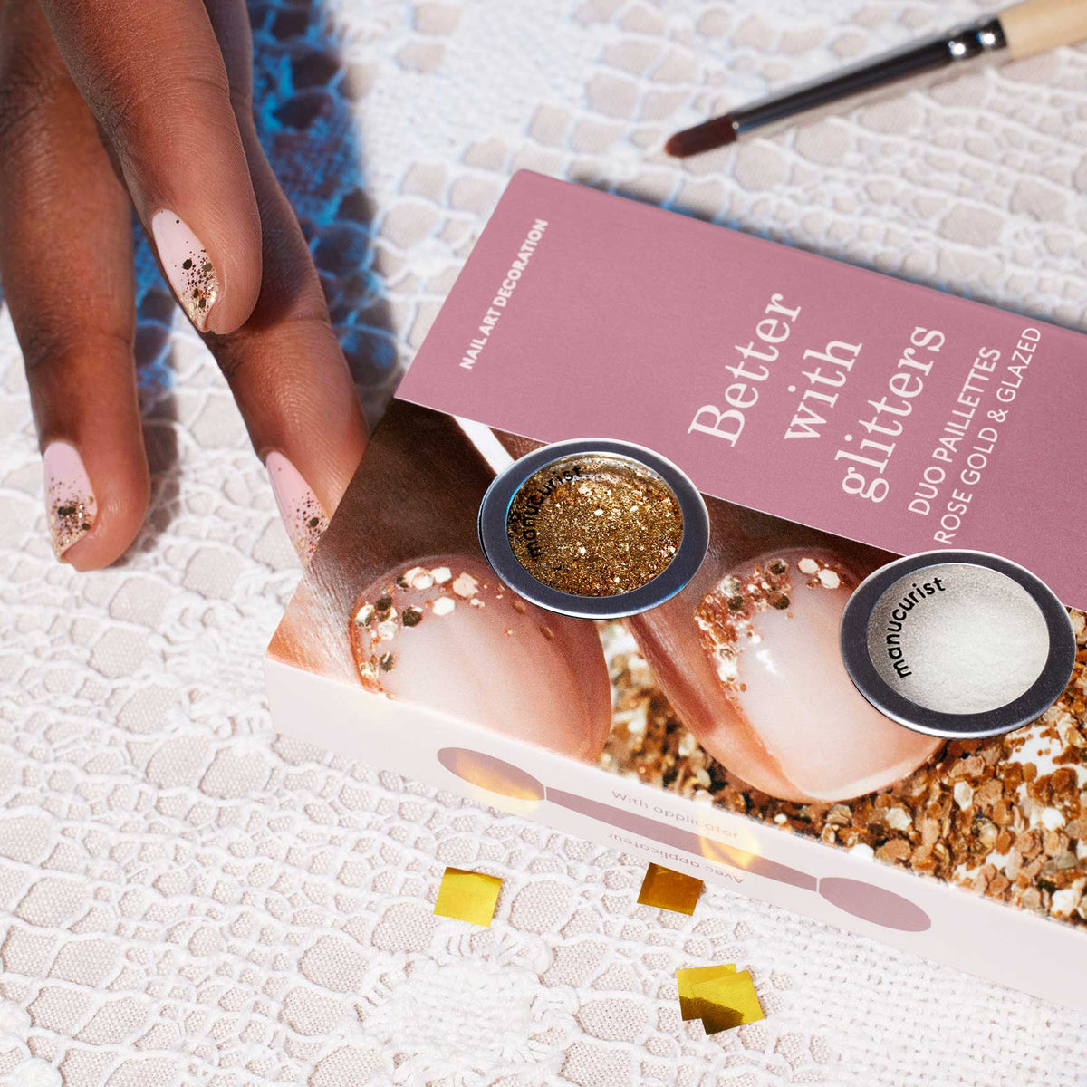 Une main aux ongles nude, ornée du Duo Paillettes Rose Gold Glazed de Manucurist, repose sur de la dentelle à côté d&