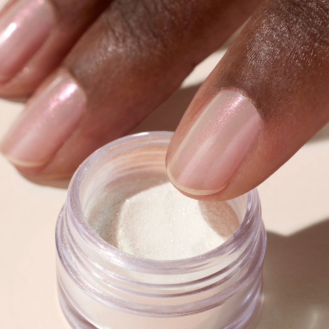 A hand with shimmery pale pink nails dips a finger into a small jar of fine, shimmery white powder from the Manucurist-test Welcome kit Nail Art.