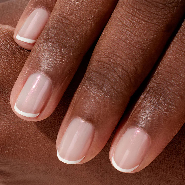 A close-up of a hand with neatly manicured nails featuring a classic French manicure—pale pink polish with thin white tips—on medium to dark skin.
