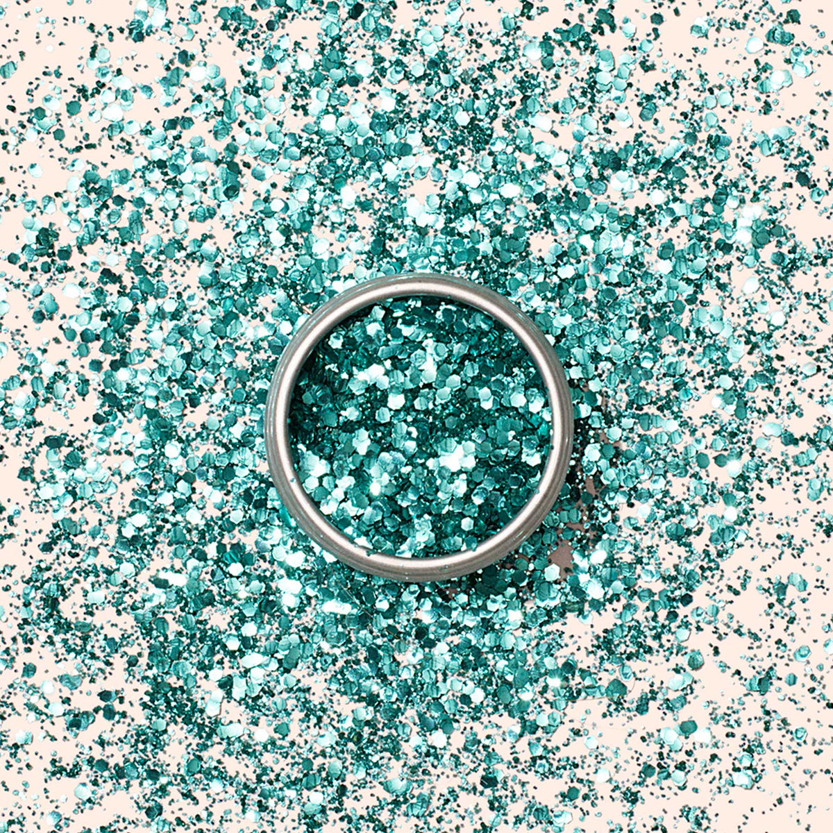 A silver ring sits on a surface sprinkled with Manucurist Turquoise Biodegradable Glitter, creating a sparkling, festive backdrop perfect for nail art inspiration.