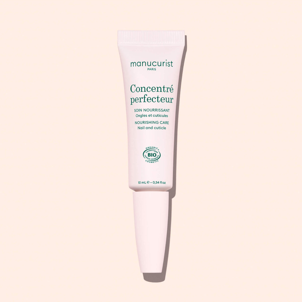 A white tube of Manucurist Nourishing Nail Pen - Cosmos Organic with green text stands upright against a light pink background—ideal for nail and cuticle care.