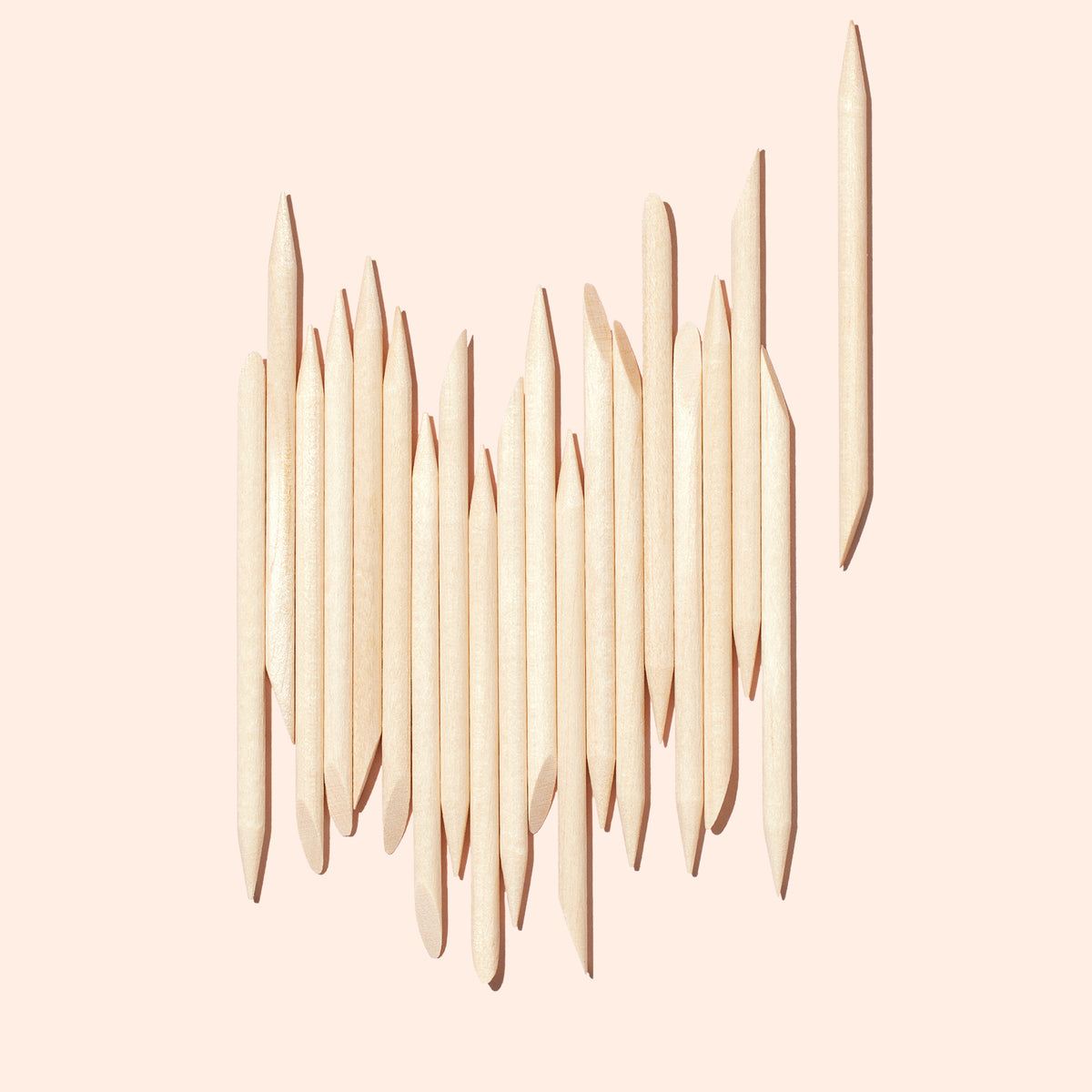 Un lot de 20 bâtonnets repousse-cuticules en bois Manucurist disposés verticalement sur un fond rose clair, avec un bâtonnet isolé sur la droite illustrant leur utilisation pour nettoyer les ongles.