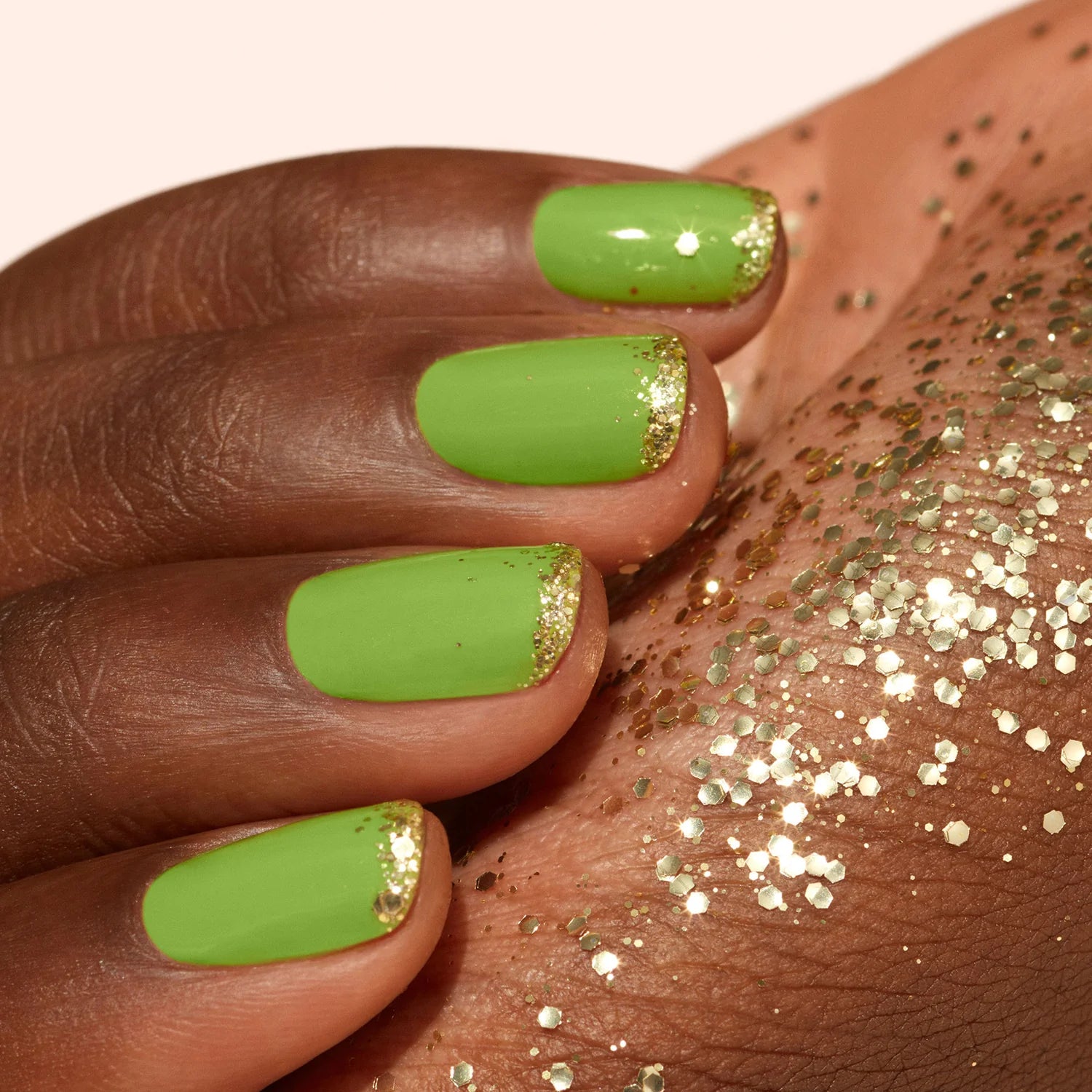 A hand with green nail polish and gold glitter tips rests on skin sprinkled with gold glitter.