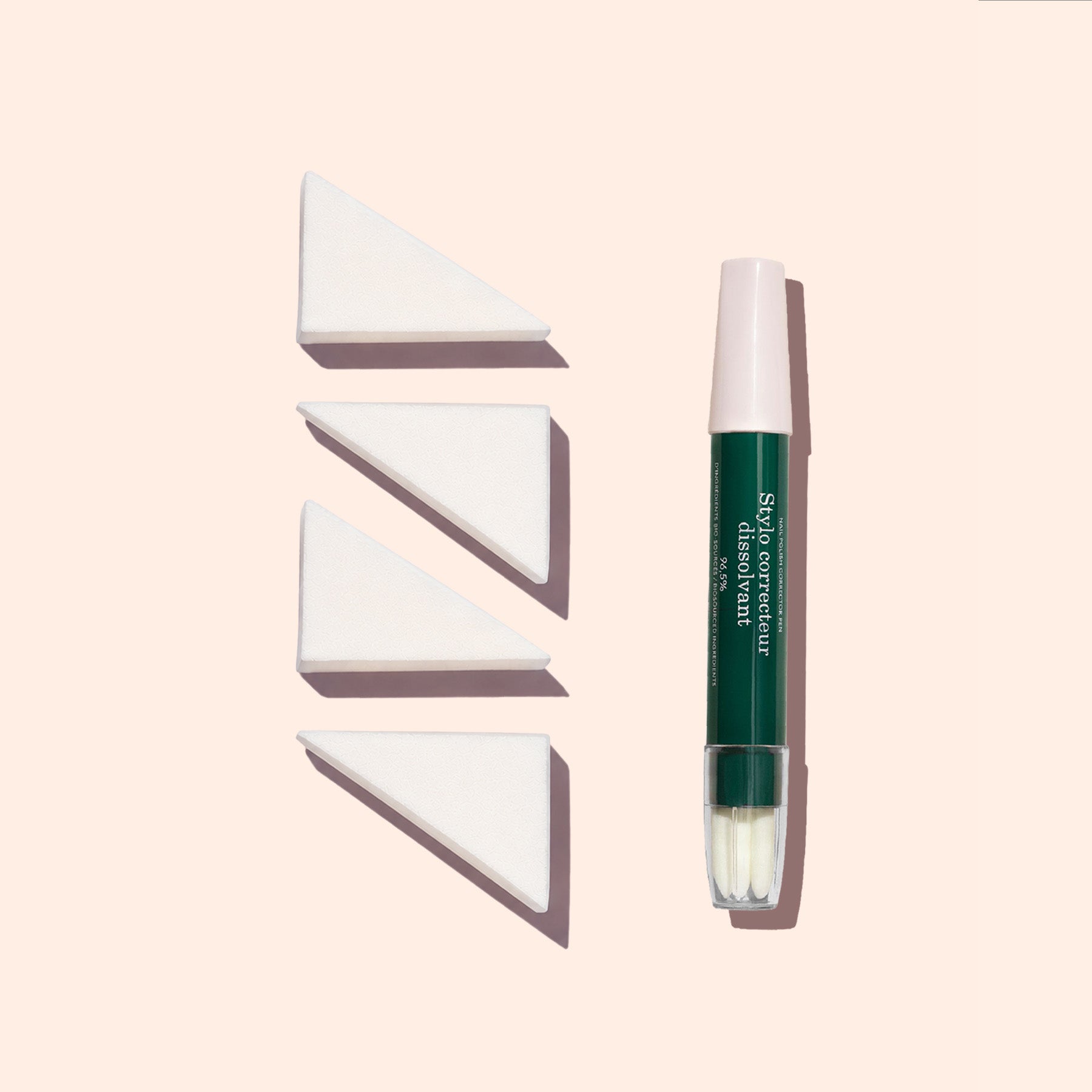A green and pink capped makeup brush stands upright next to three Manucurist Nail Art Sponges (set of 4) arranged in a row on a light beige background.