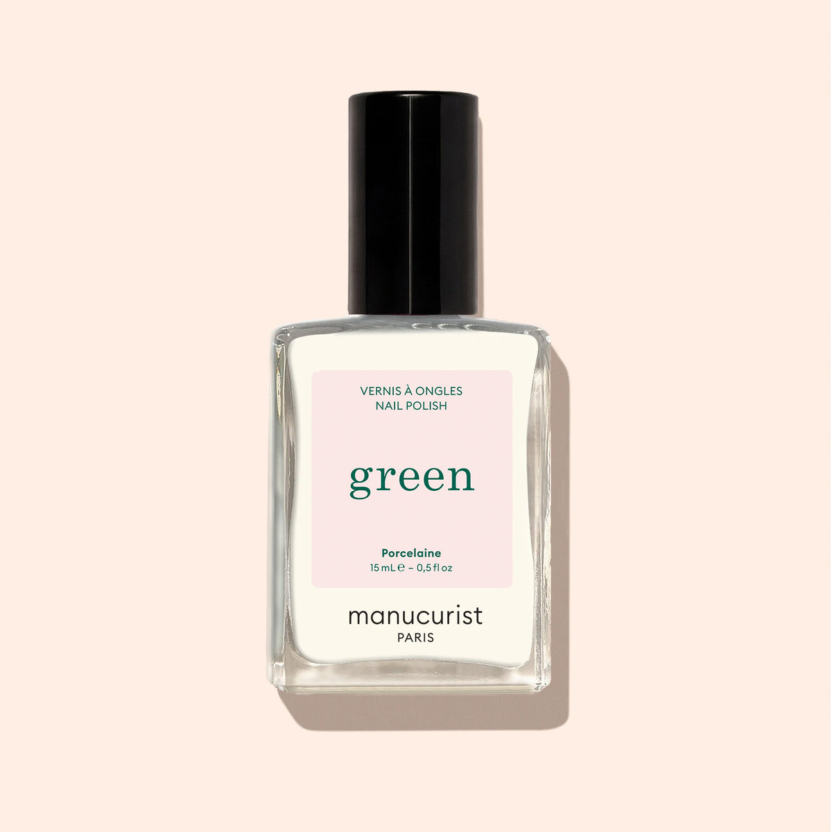 Un flacon en verre transparent de vernis à ongles Porcelaine Manucurist au bouchon noir, avec la mention "Quick Dry Intense Color", est présenté sur un fond beige clair.