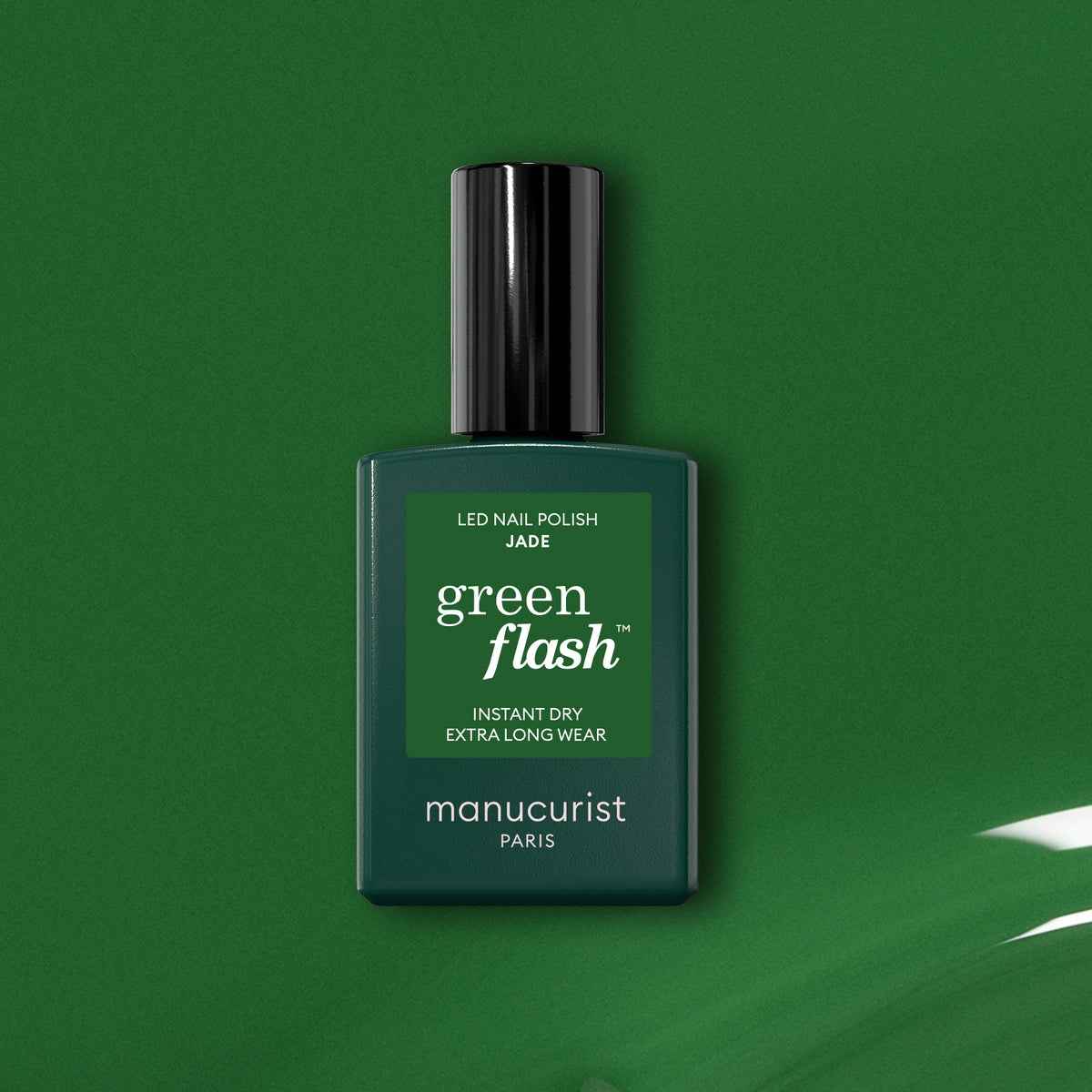 Un flacon de vernis à ongles LED Green Flash Jade Manucurist posé sur un fond vert, avec un trait de vernis vert brillant dans le coin inférieur droit.