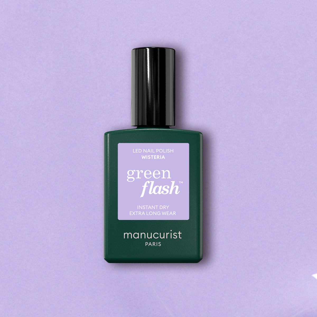 Un flacon de Wisteria Manucurist est posé sur un fond lavande clair. Le flacon vert foncé présente une étiquette lavande et un bouchon noir, mettant en avant ce vernis gel violet pastel de la gamme Green Flash compatible LED de la marque.