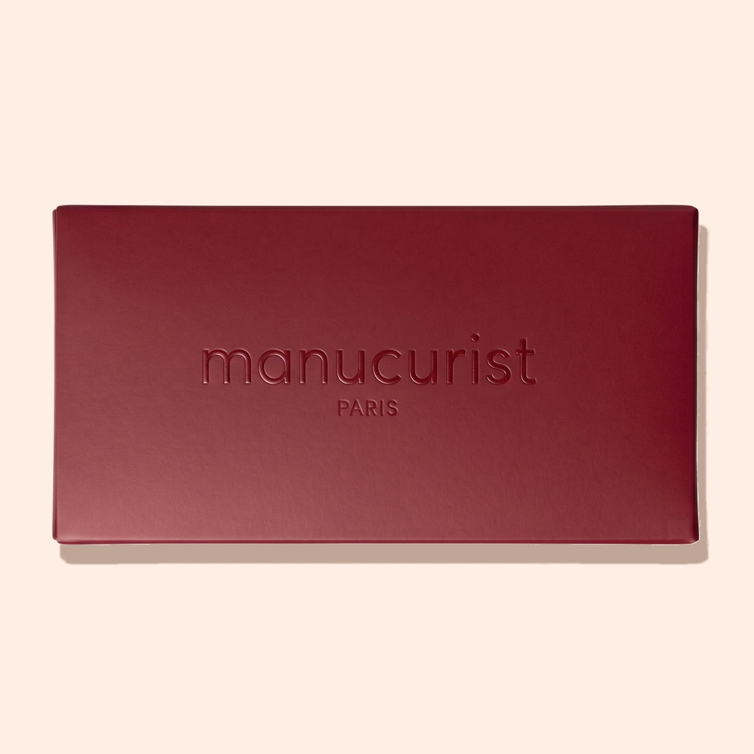 A closed, rectangular Burgundy Holiday Rainbow Box by Manucurist, with the brand name and “PARIS” embossed on the lid, set against a light beige background.
