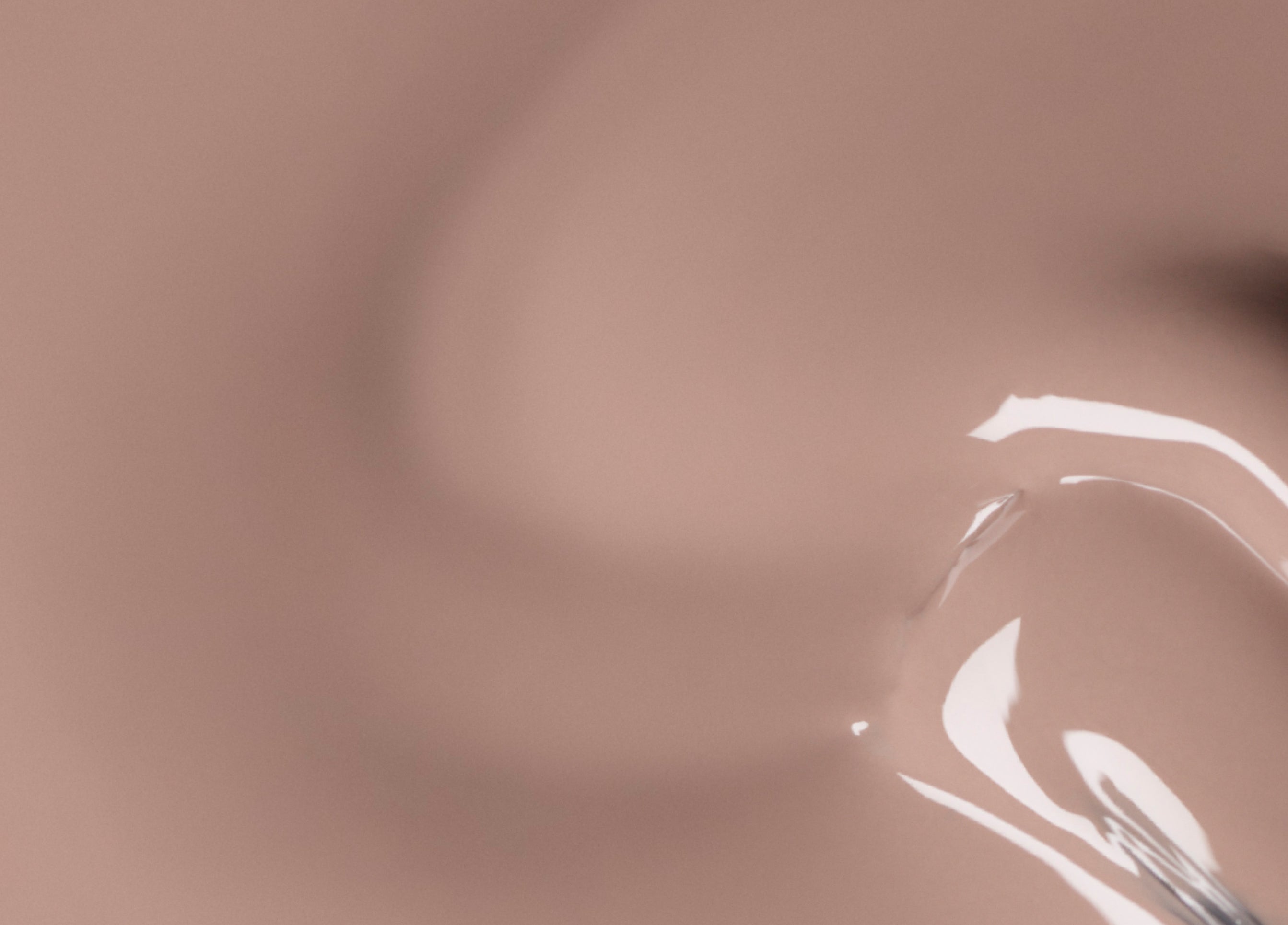 Close-up of a smooth, glossy surface in light beige tones with reflective highlights and soft, abstract curves.