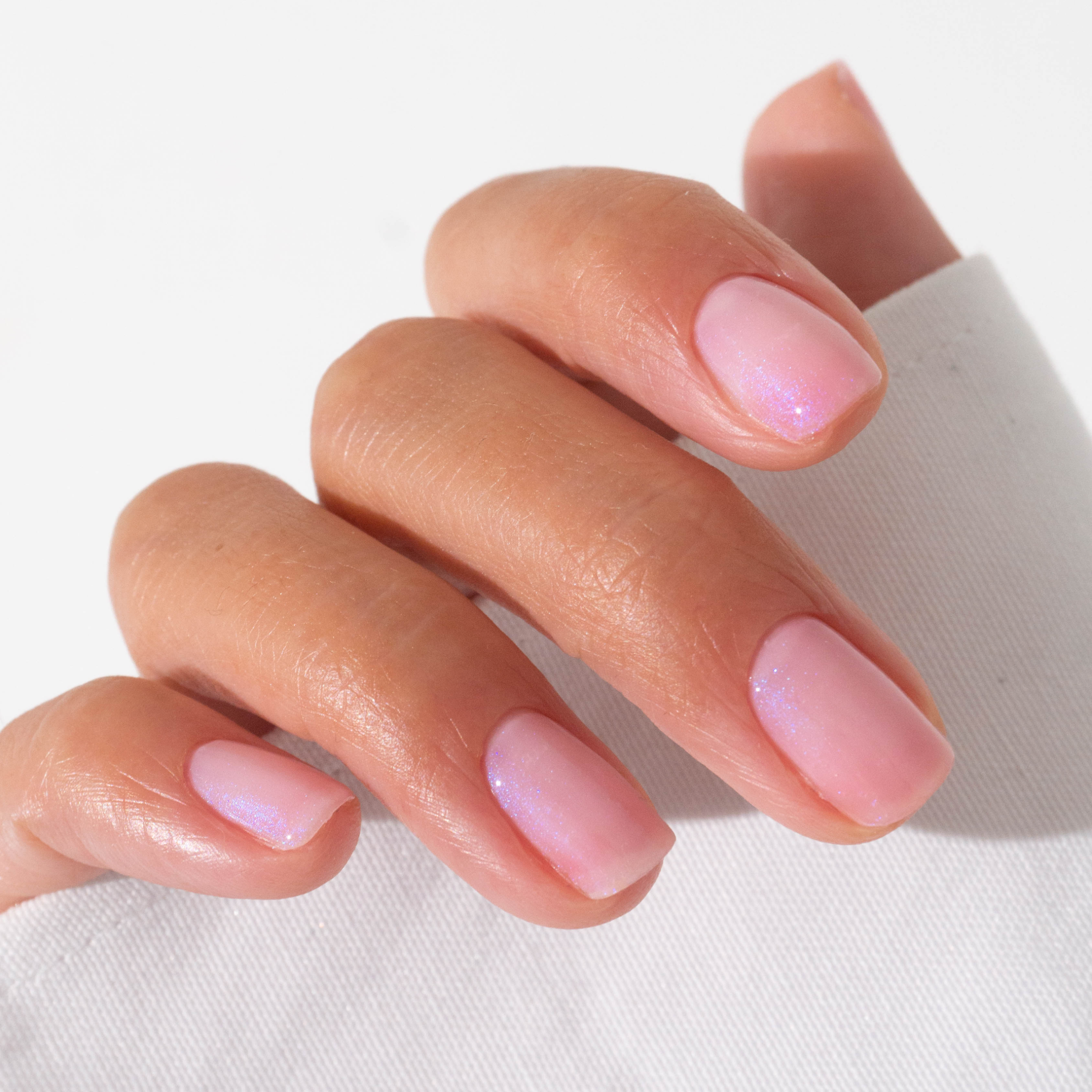 A hand with neatly manicured nails painted with shiny, light pink nail polish, resting on a white surface.