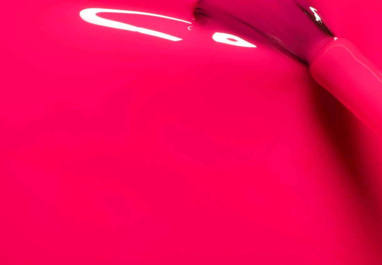 A close-up of a brush applying bright pink nail polish, with glossy streaks and reflections visible on the smooth surface.