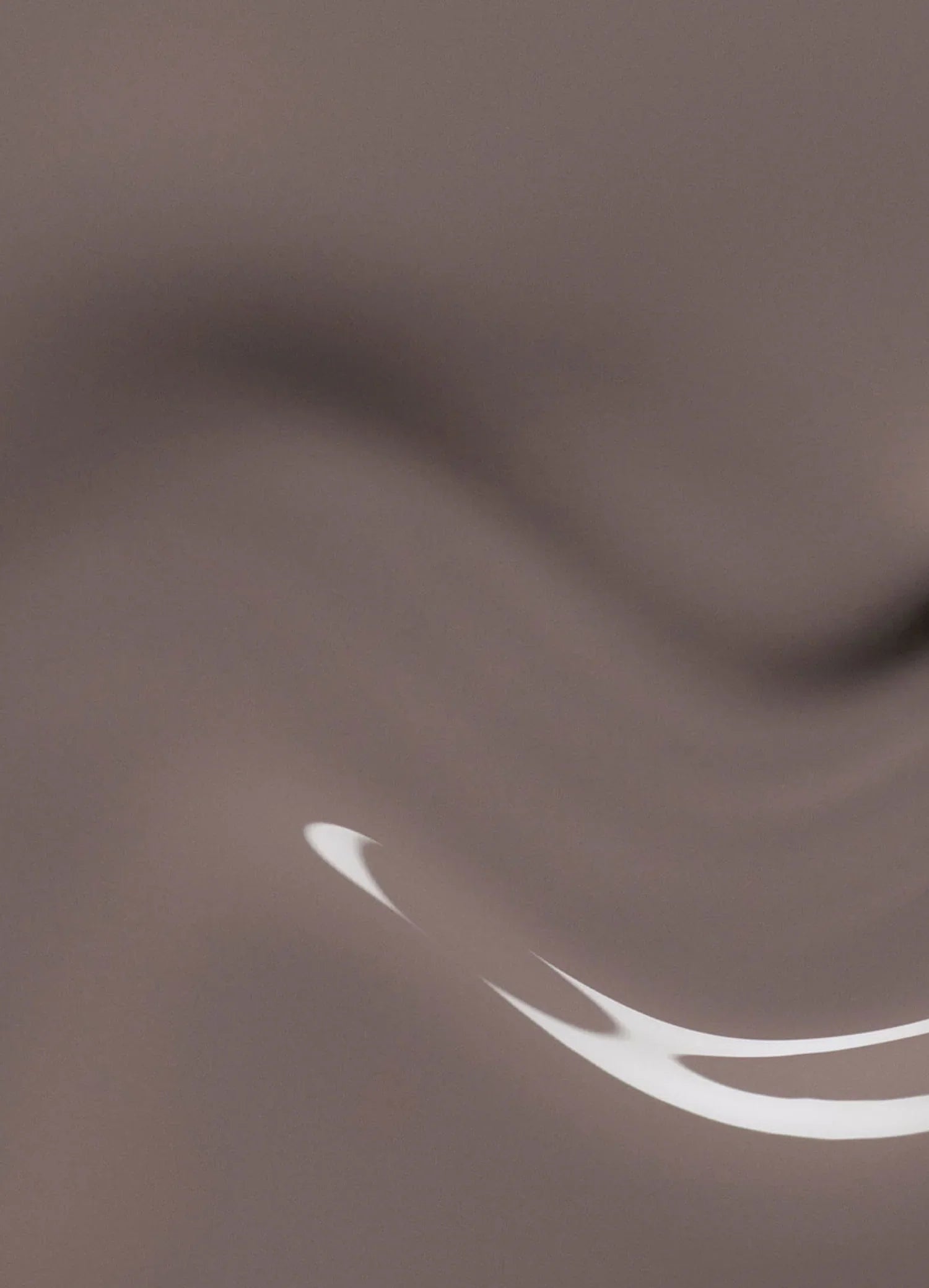 A smooth, abstract surface in shades of light brown with gentle waves and a curved reflection of white light in the lower right corner.