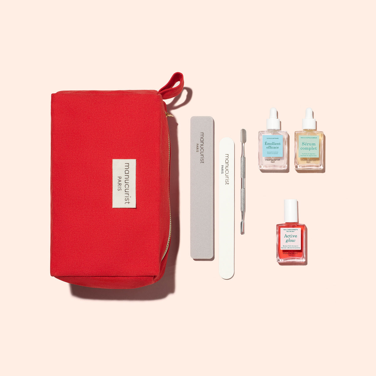 Le Healthy Glow Duo de Manucurist est présenté avec une pochette rouge zippée, une lime à ongles grise, un polissoir blanc, un repousse-cuticules en métal et trois flacons, dont du vernis à ongles et de l’huile pour cuticules, disposés sur un fond beige.