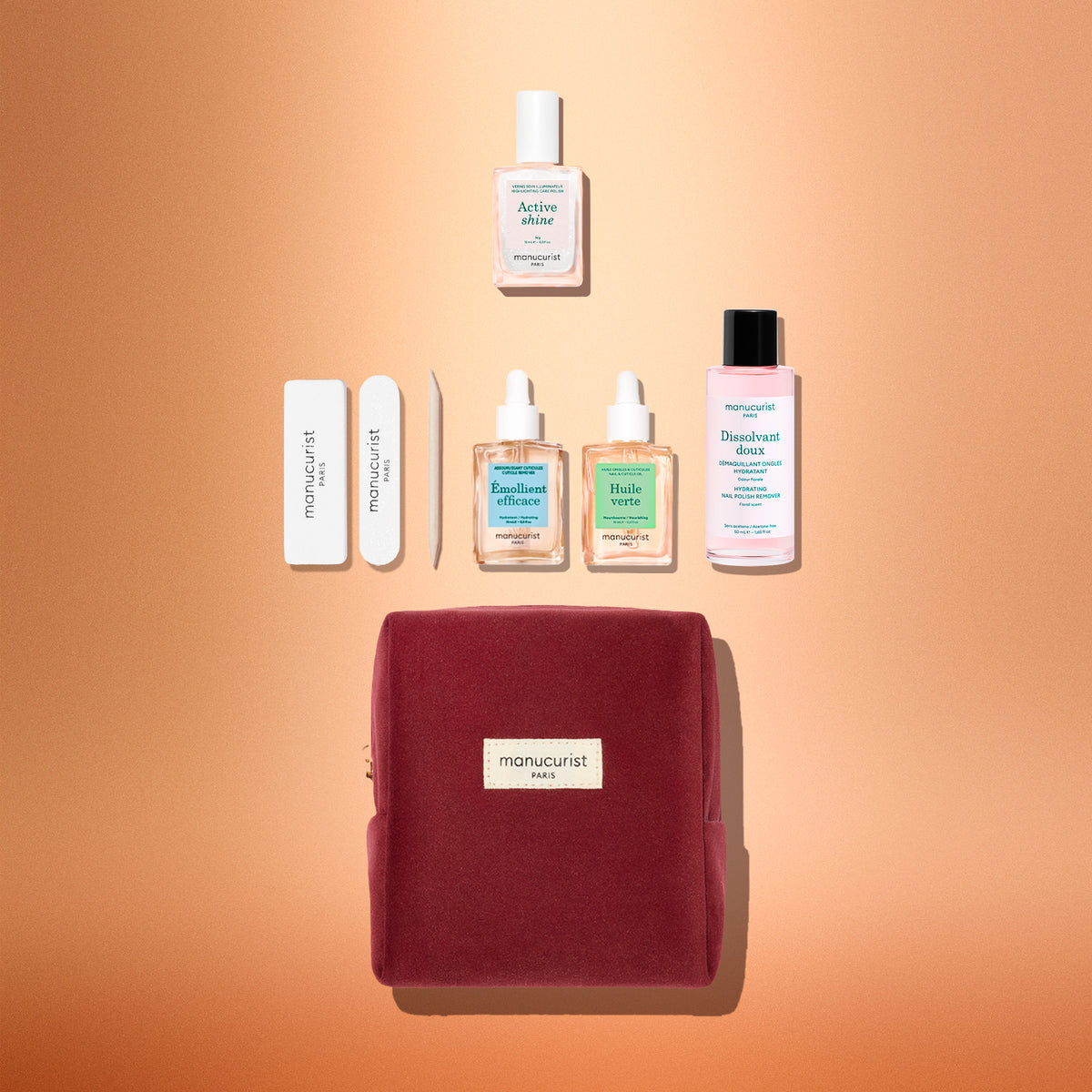 Experience the Manucurist Active™ Discovery Gift Set: a beautifully arranged collection featuring two nail files, two cuticle oils, a cuticle remover, a nail strengthener, and a bottle of nail polish remover—all presented in an elegant burgundy pouch on a peach background. Perfect for elevating your manicure routine and achieving stunning nails.